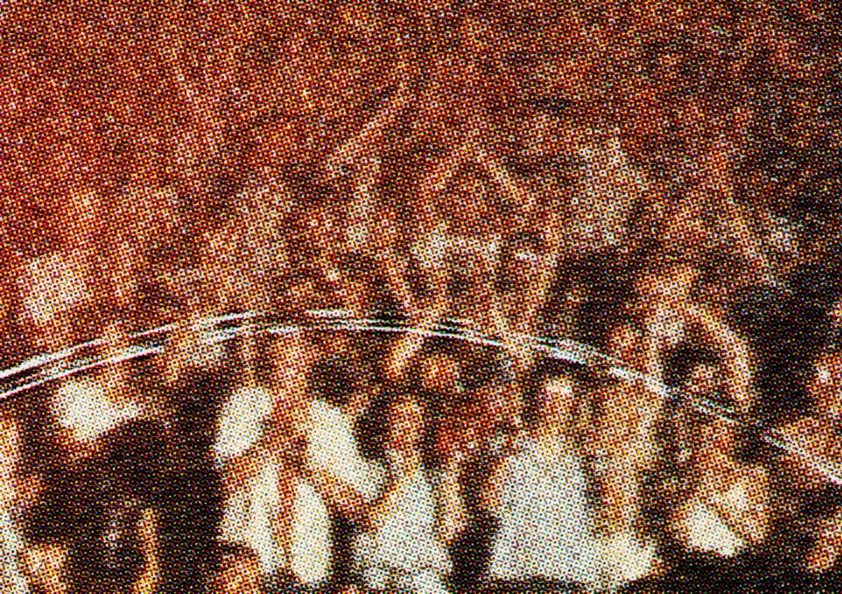 Crowd of concert-goers with raised hands at a live performance in a dim venue.