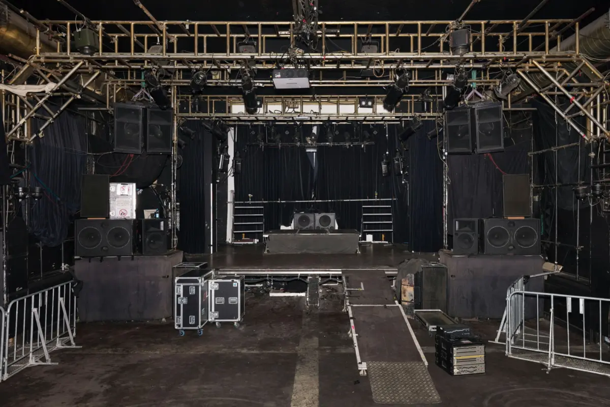 Empty concert stage being prepared with speaker stacks, lighting truss, ramps, and road cases.