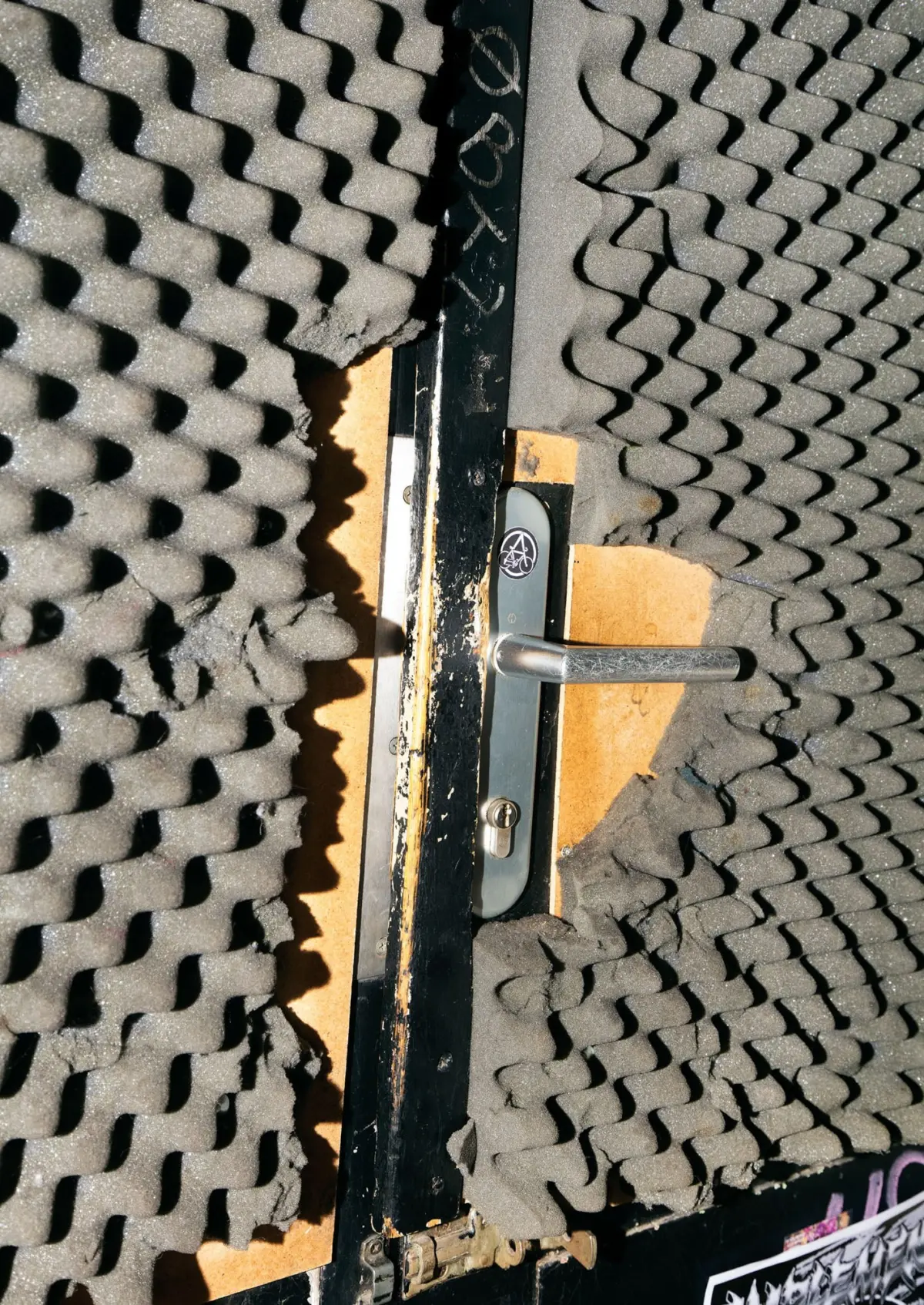 Metal lever door handle on a door surrounded by egg-crate acoustic foam panels.