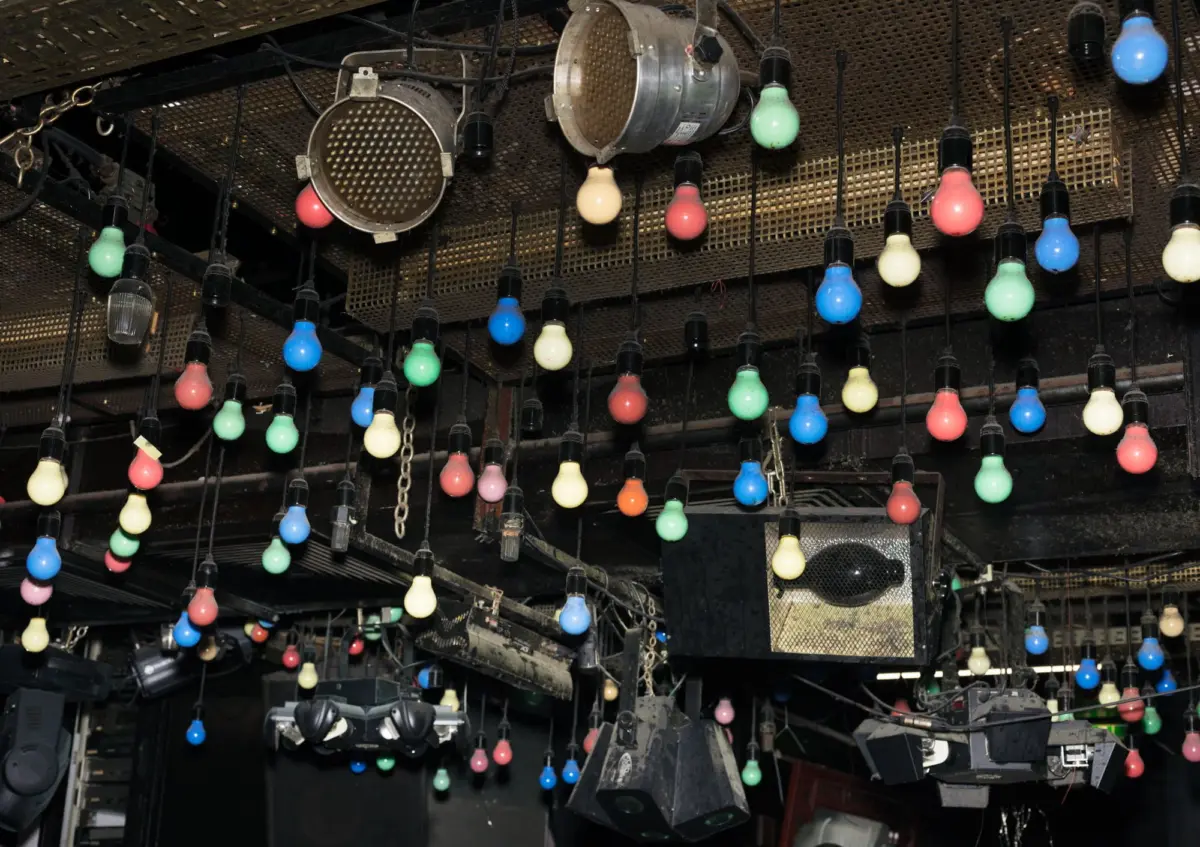 theater stage lighting rig with numerous colorful hanging bulbs, metal grid, and overhead spotlights.