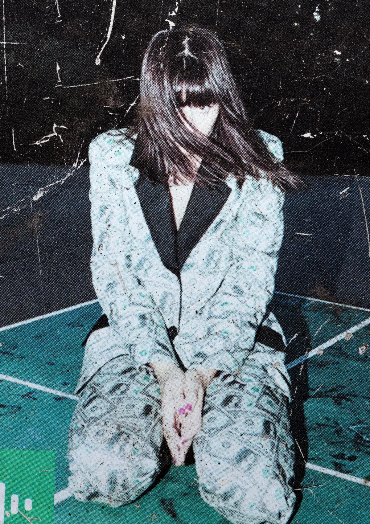 Person kneeling on a teal floor, wearing a light patterned suit; hair obscures face, hands clasped in front.