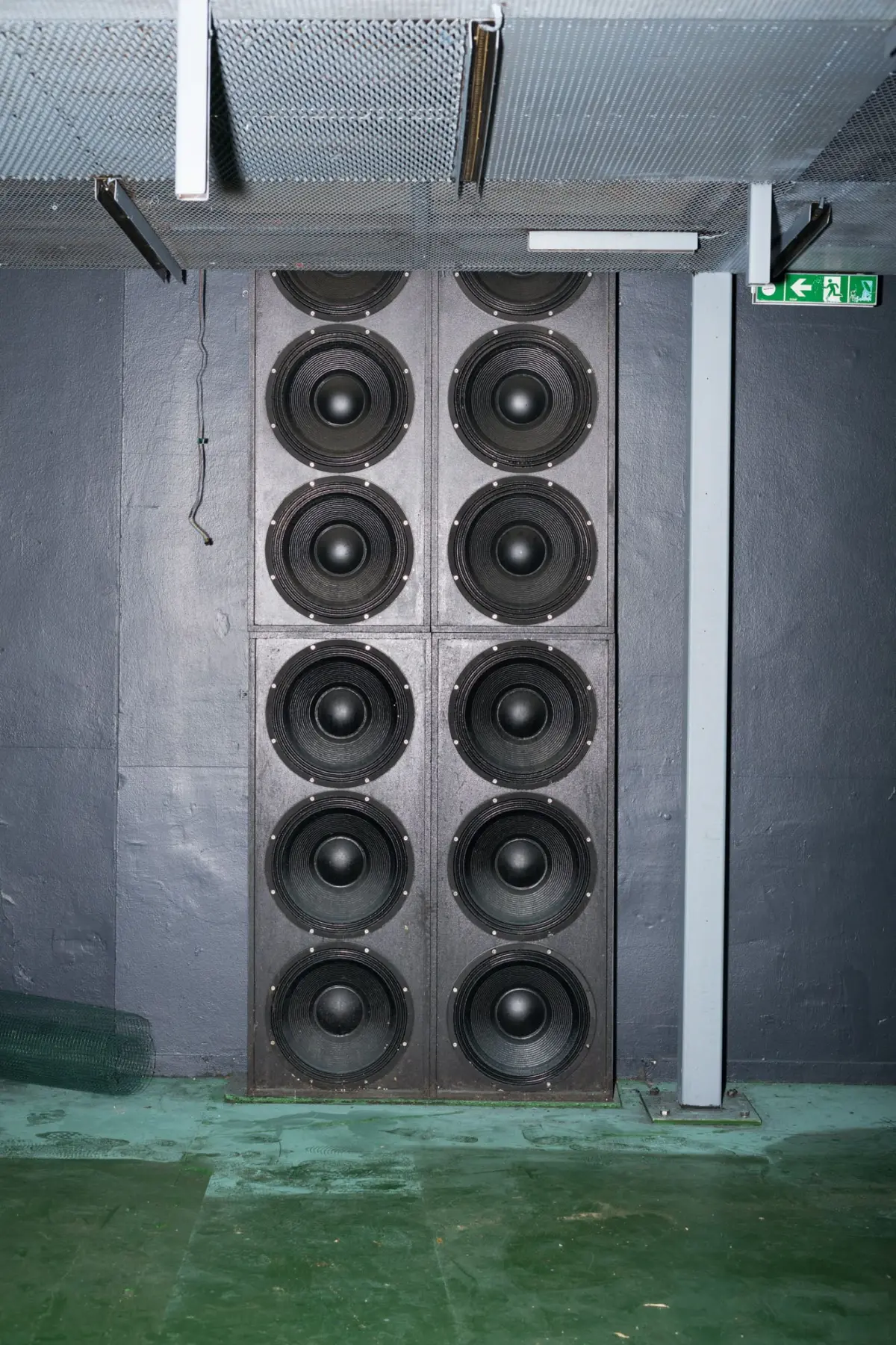 Tall two-column loudspeaker array with ten drivers mounted against a gray wall in an industrial room.
