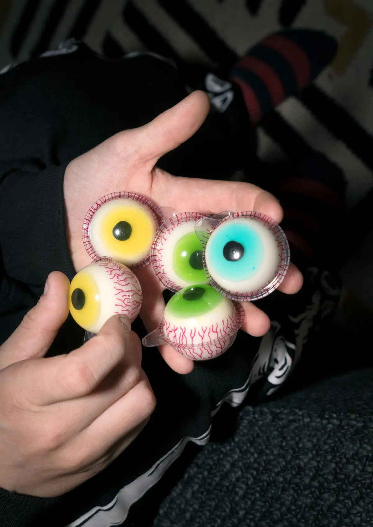 Hands holding several plastic eyeballs with red-veined sclera and colorful yellow, green, and blue irises on a person's lap.