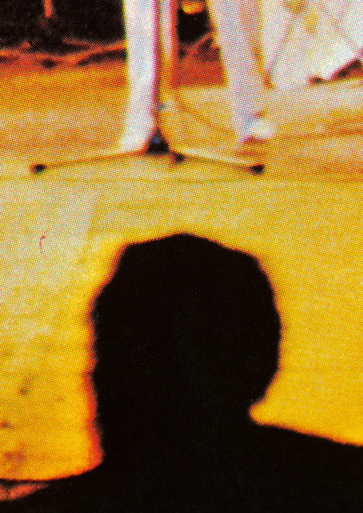 Silhouette of a person seen from behind on a bright yellow stage, with two figures in white pants in the background.