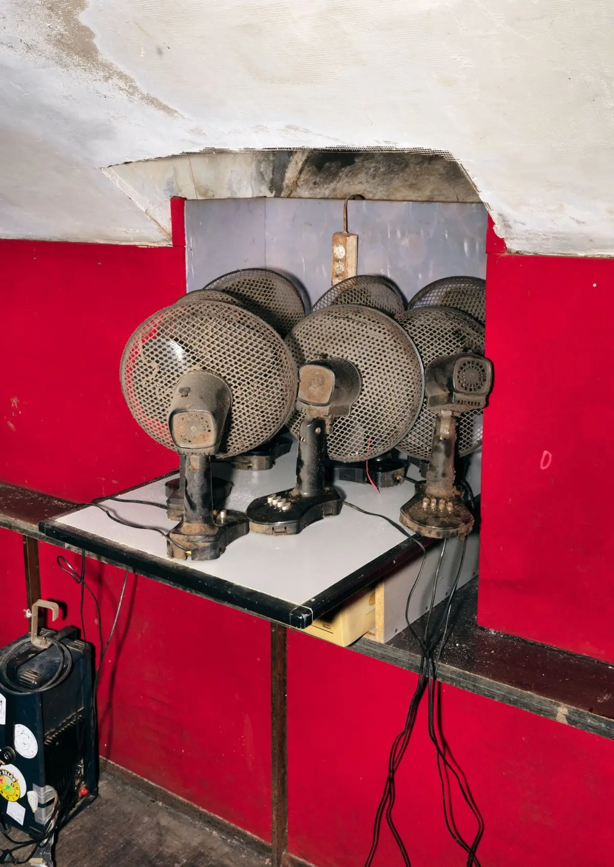 Row of dusty circular metal-mesh fans resting on a white worktable in a red-walled workshop.