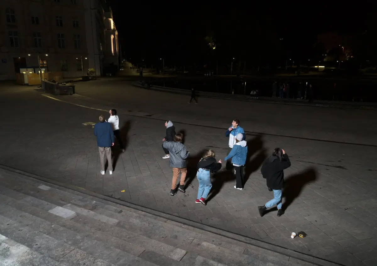 Group of people in casual clothing forming a circle on a lit plaza at night beside a canal