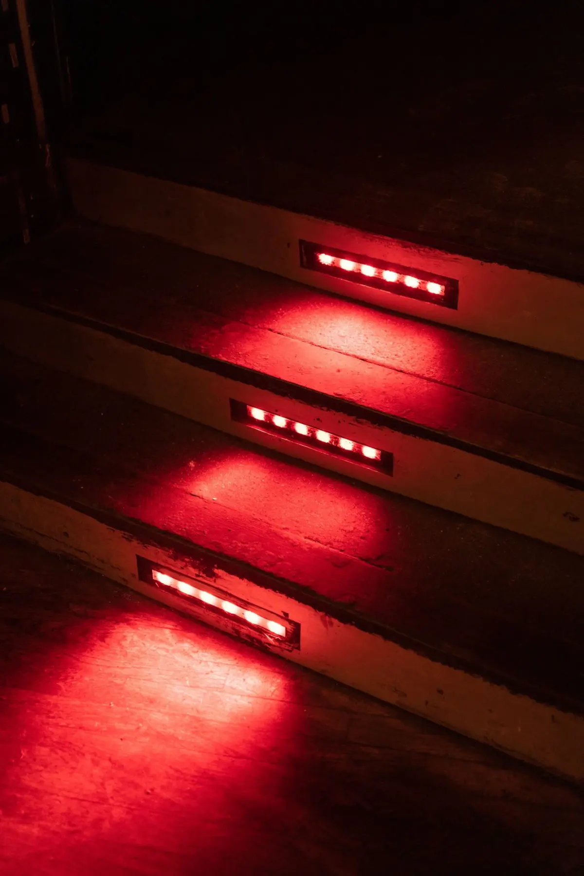 Dimly lit wooden staircase with red rectangular LED strip lights on each step.