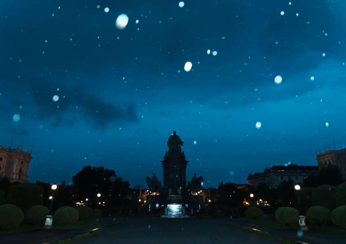 Equestrian statue standing on a pedestal in a city park at night, with illuminated lamps and neoclassical buildings in the background.