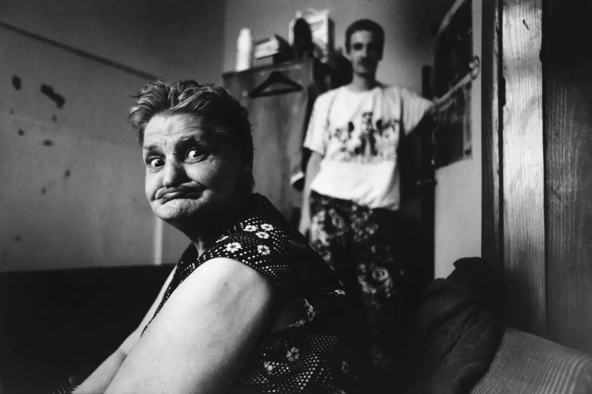Older adult person in foreground making a goofy facial expression; another person stands in doorway in background.