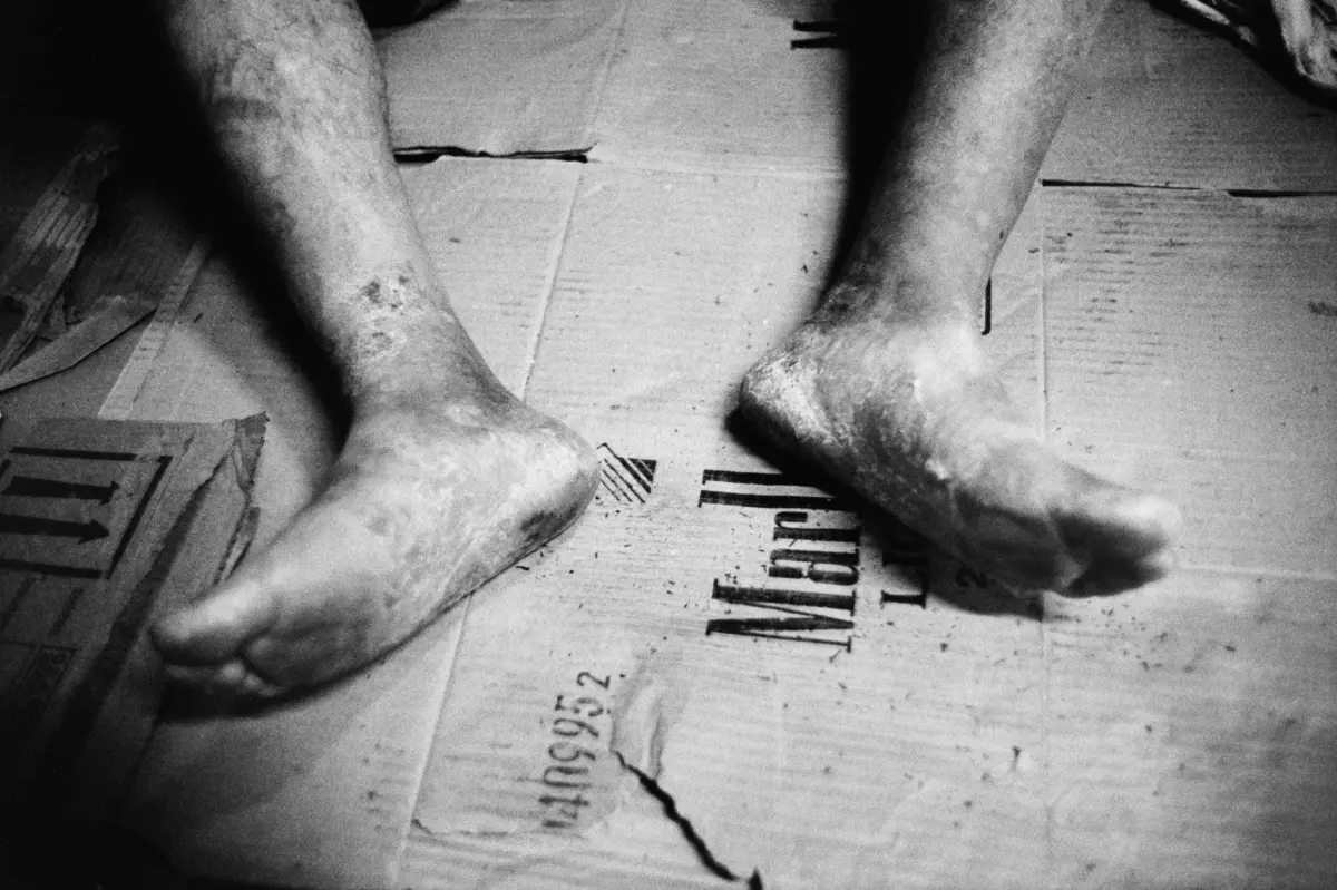 Close-up of dirty forearms and hands pressing on a torn, flattened cardboard box.