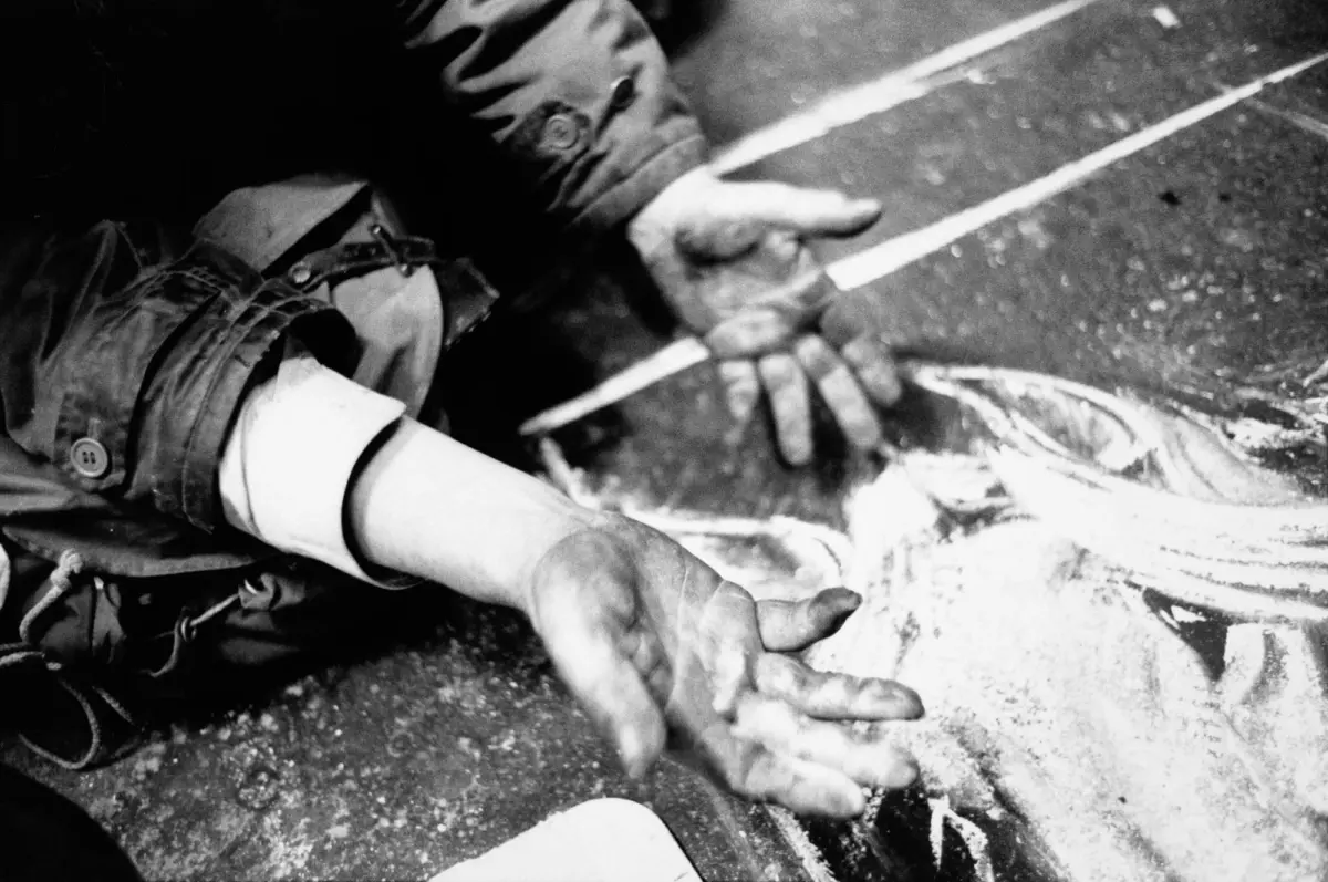 Person in a jacket draws with chalk on pavement, forming a circular design.