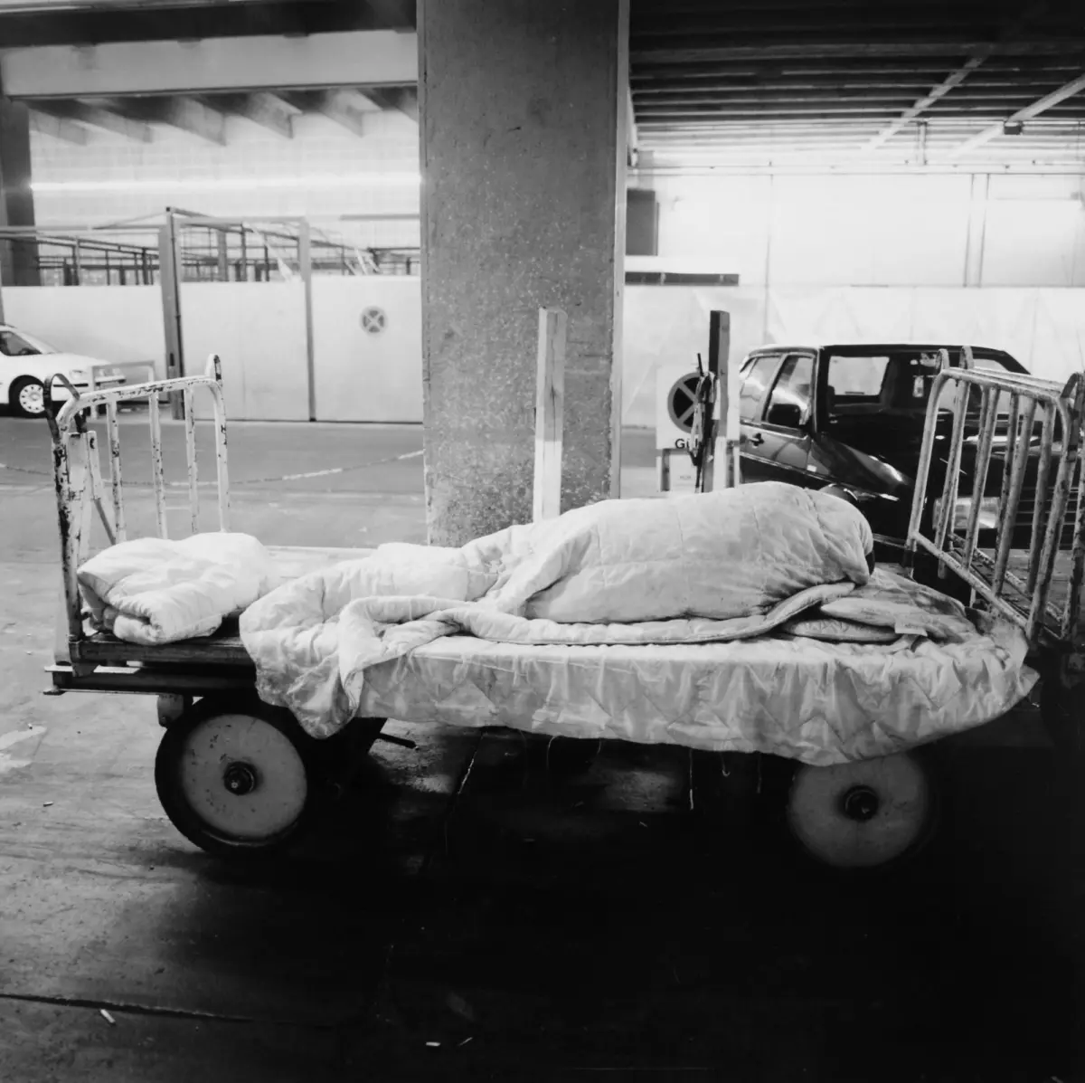 Hospital bed on wheels covered with blankets in a parking garage.