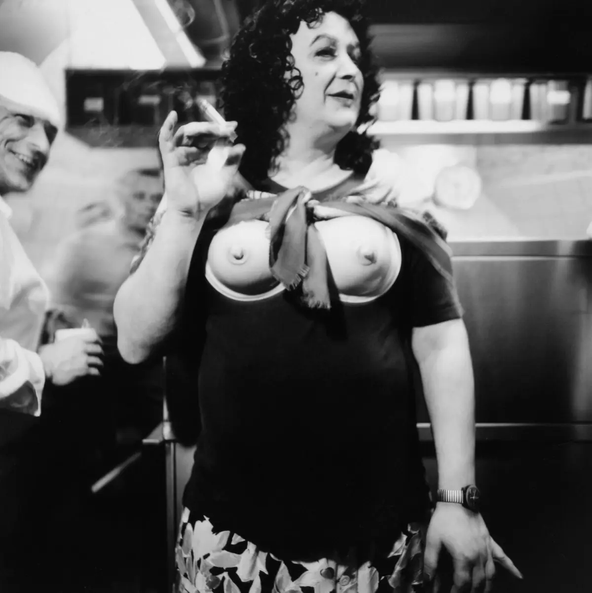 Curly-haired person smoking a cigarette in a kitchen interior.