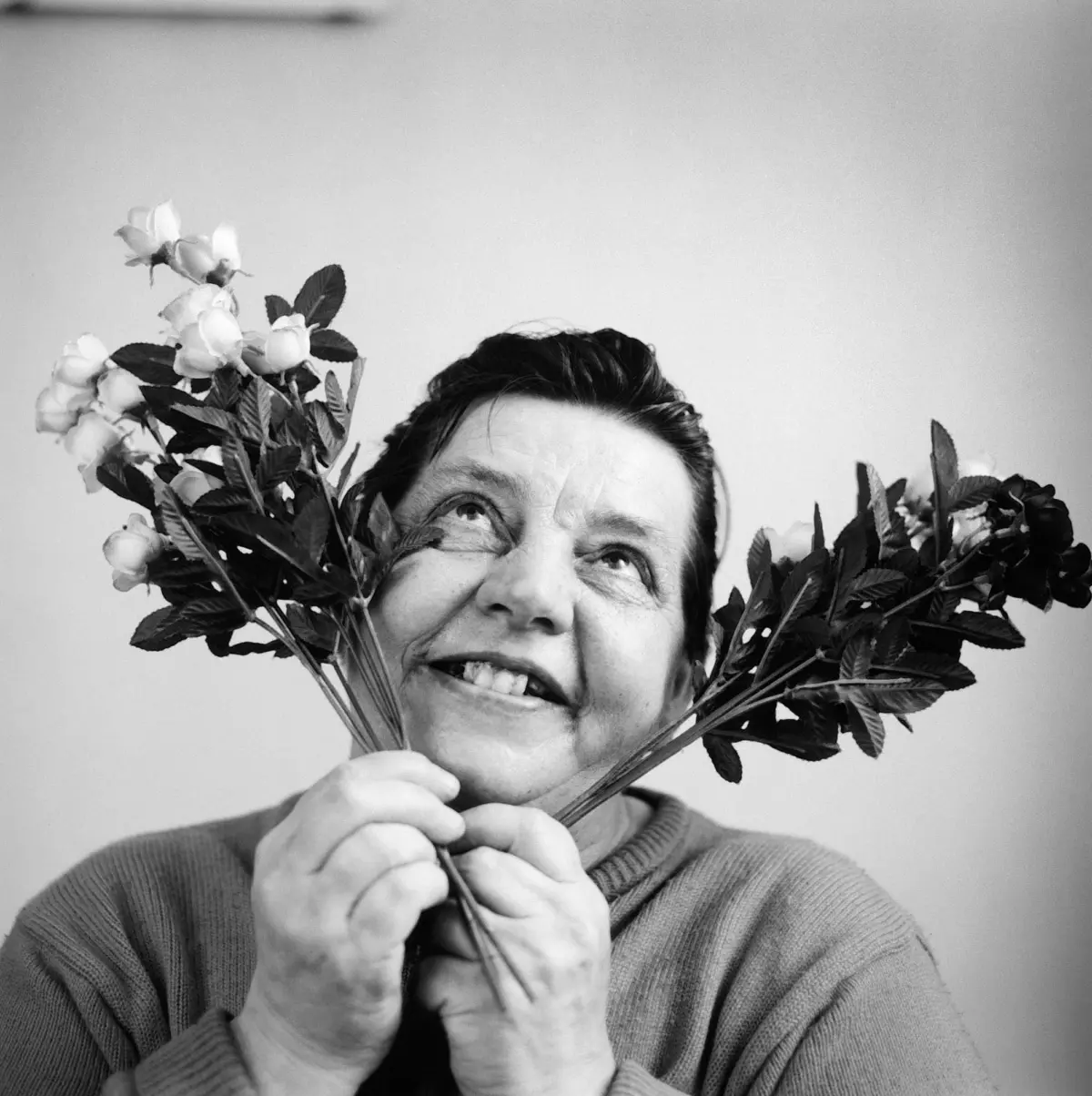 Older adult holding a bouquet of white roses in front of their face, smiling.
