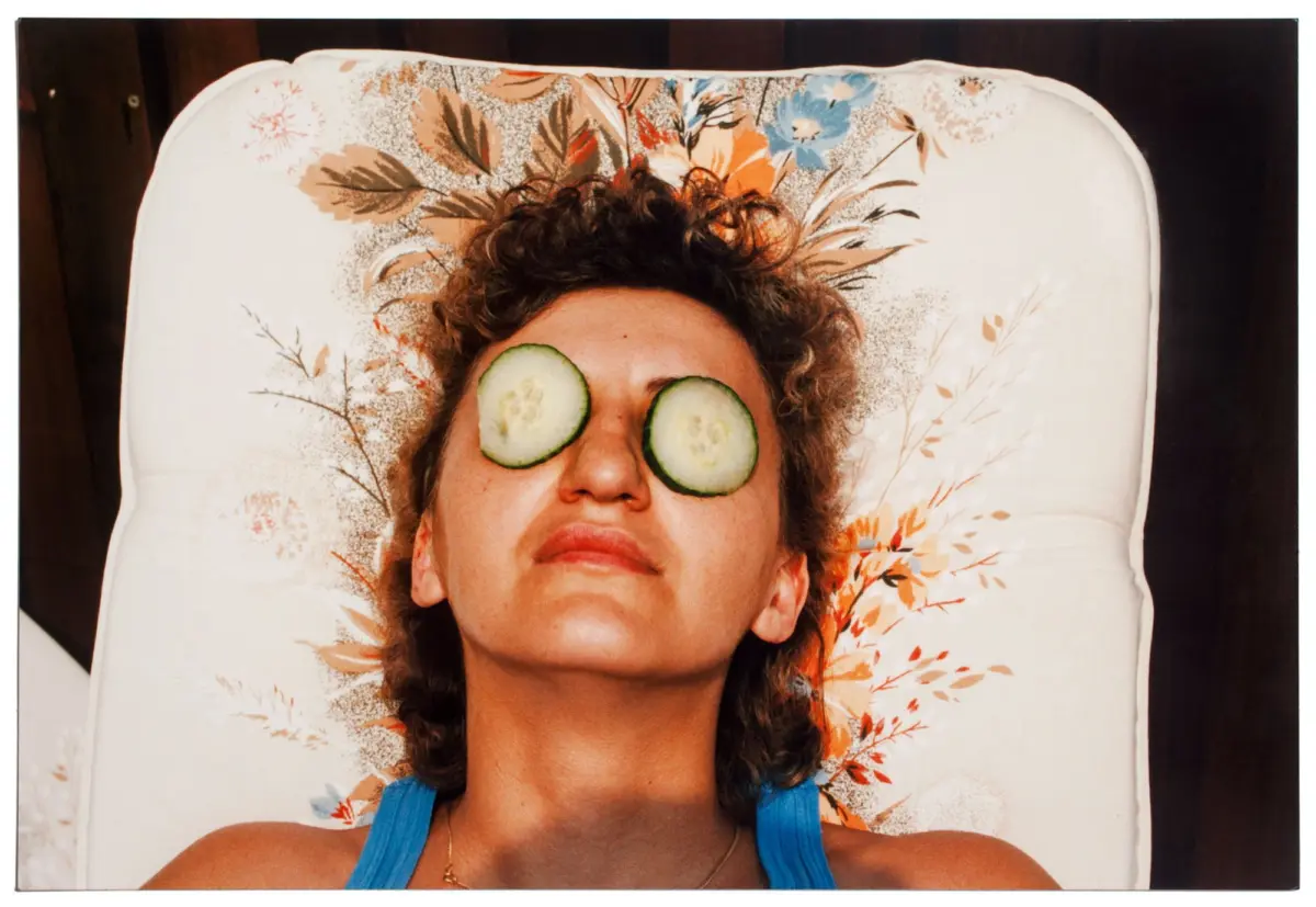 Person lying on floral-patterned pillow with cucumber slices over eyes.