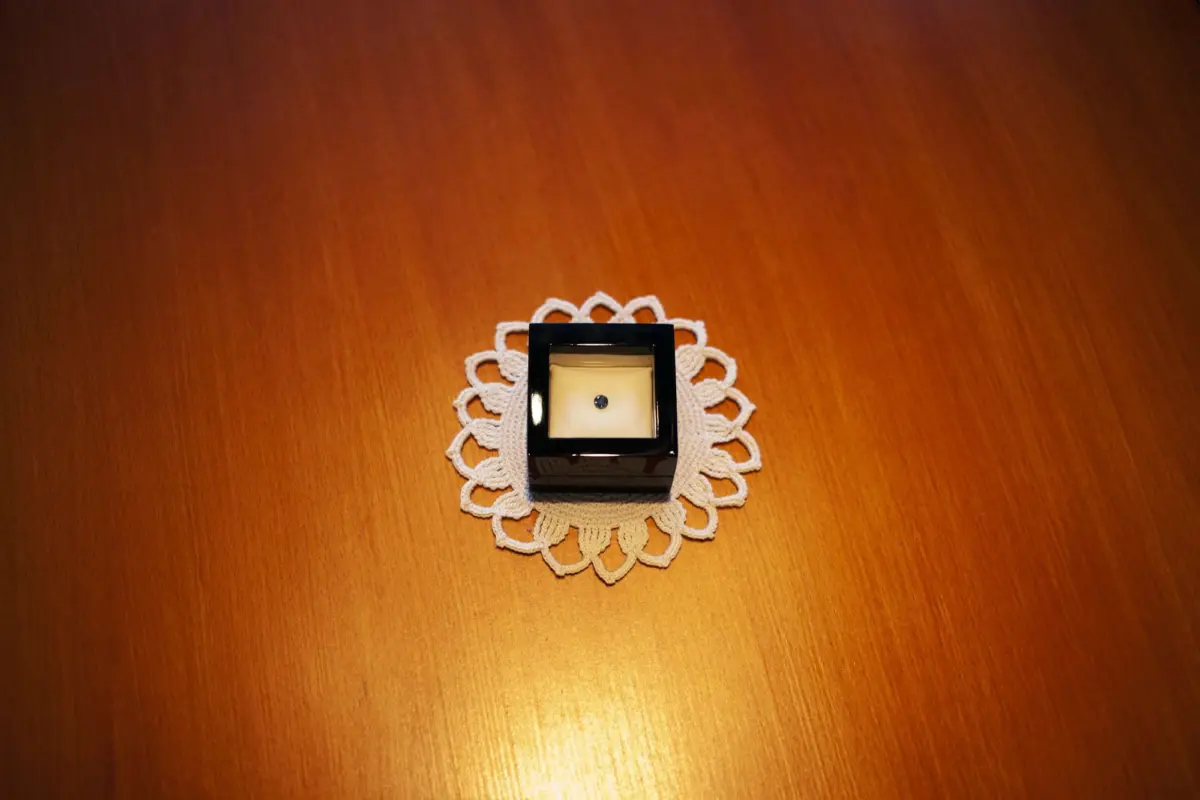Diamond ring in a black square jewelry box, resting on a white crocheted lace doily on a wooden table.