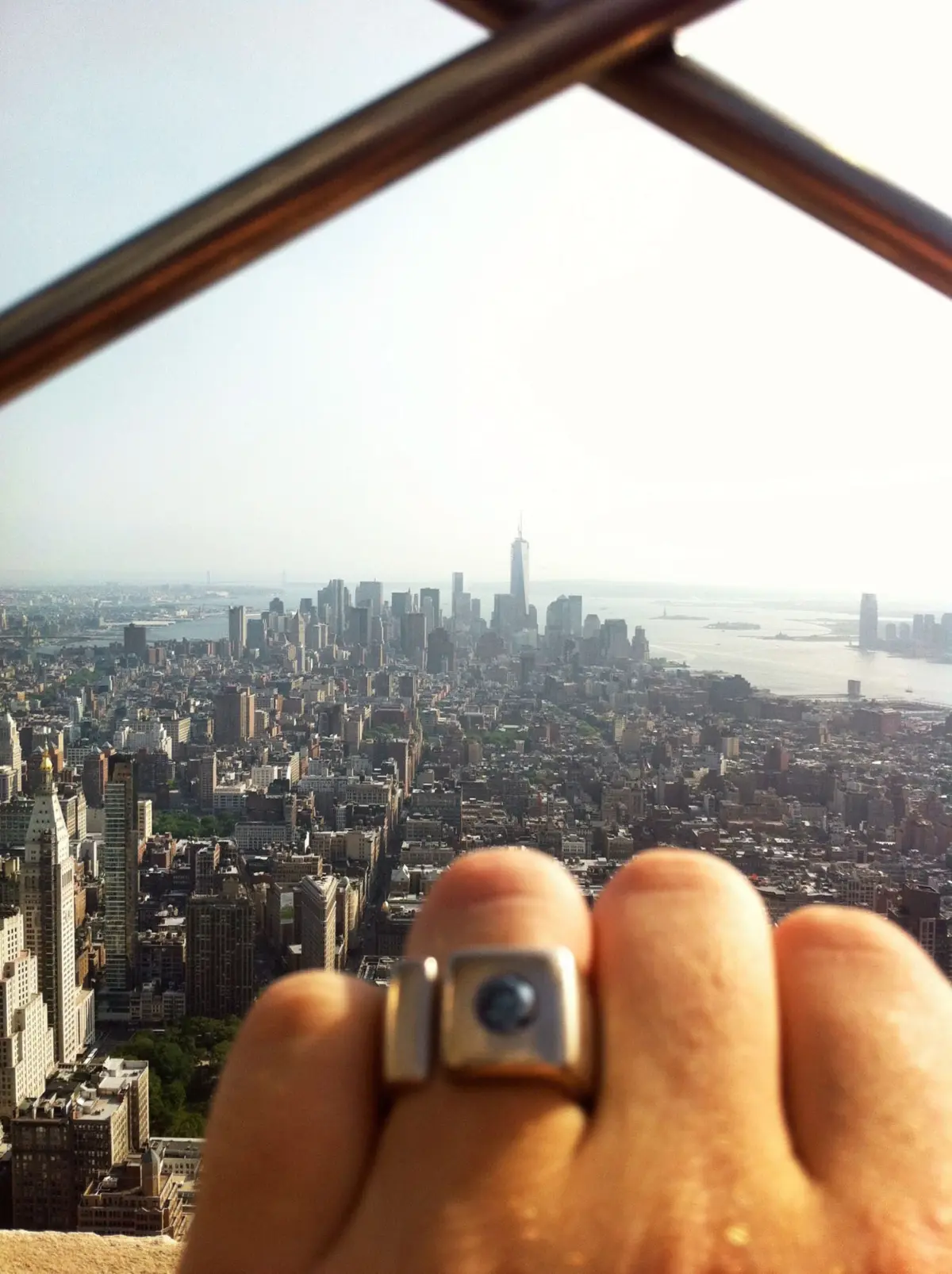 Close-up of a hand holding a small camera, aimed at the Manhattan skyline with the river beyond.
