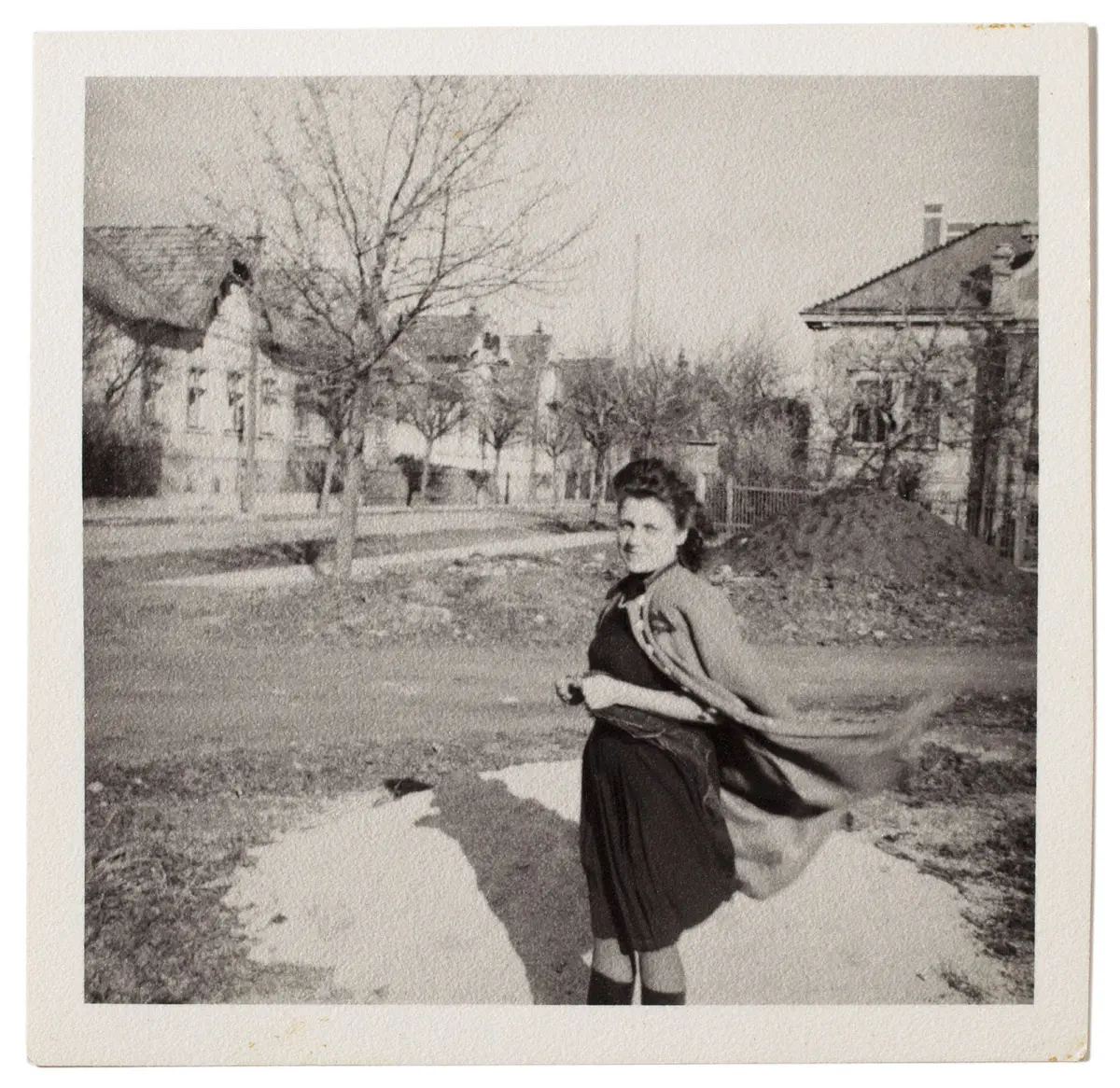 Adult person in vintage dress walking down a residential street with bare trees and houses in the background.