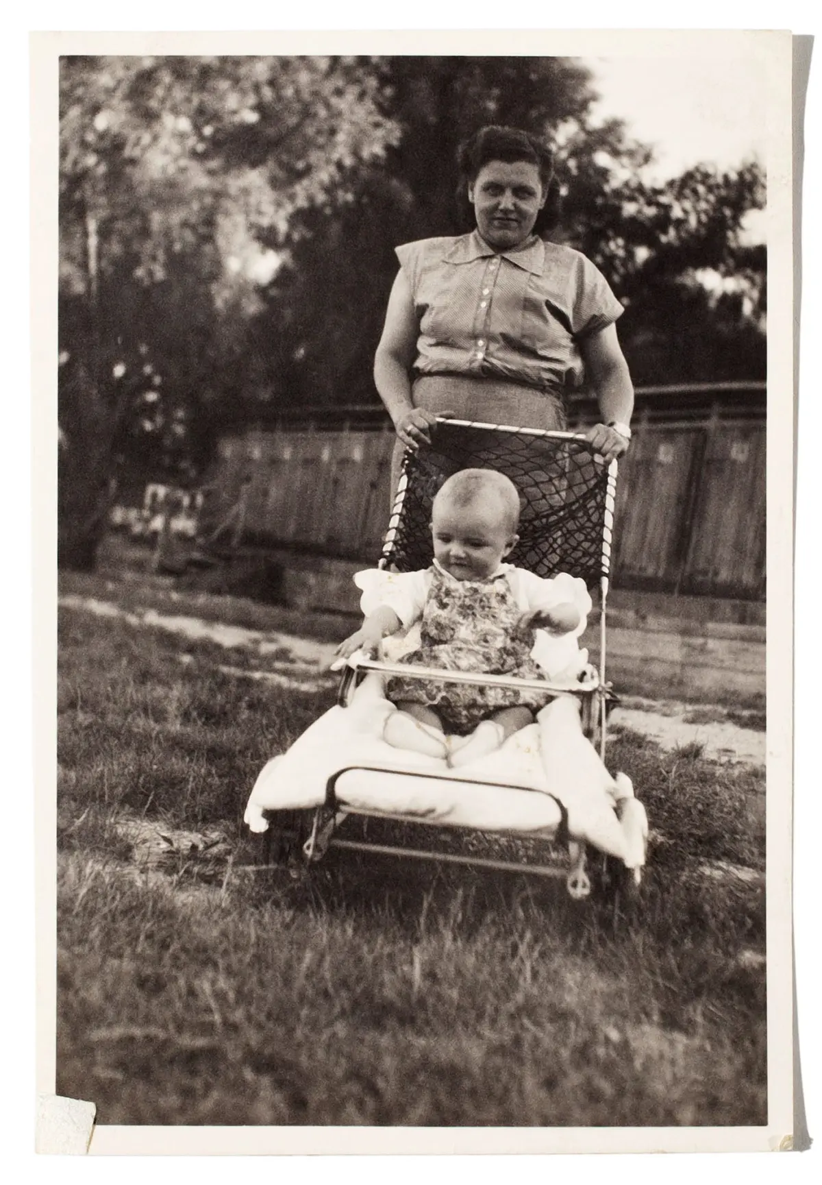 Adult pushing a baby in a vintage stroller outdoors in a grassy backyard.