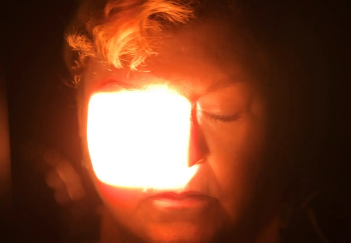 Close-up of a person's face in darkness, illuminated by a bright rectangular light near the mouth.
