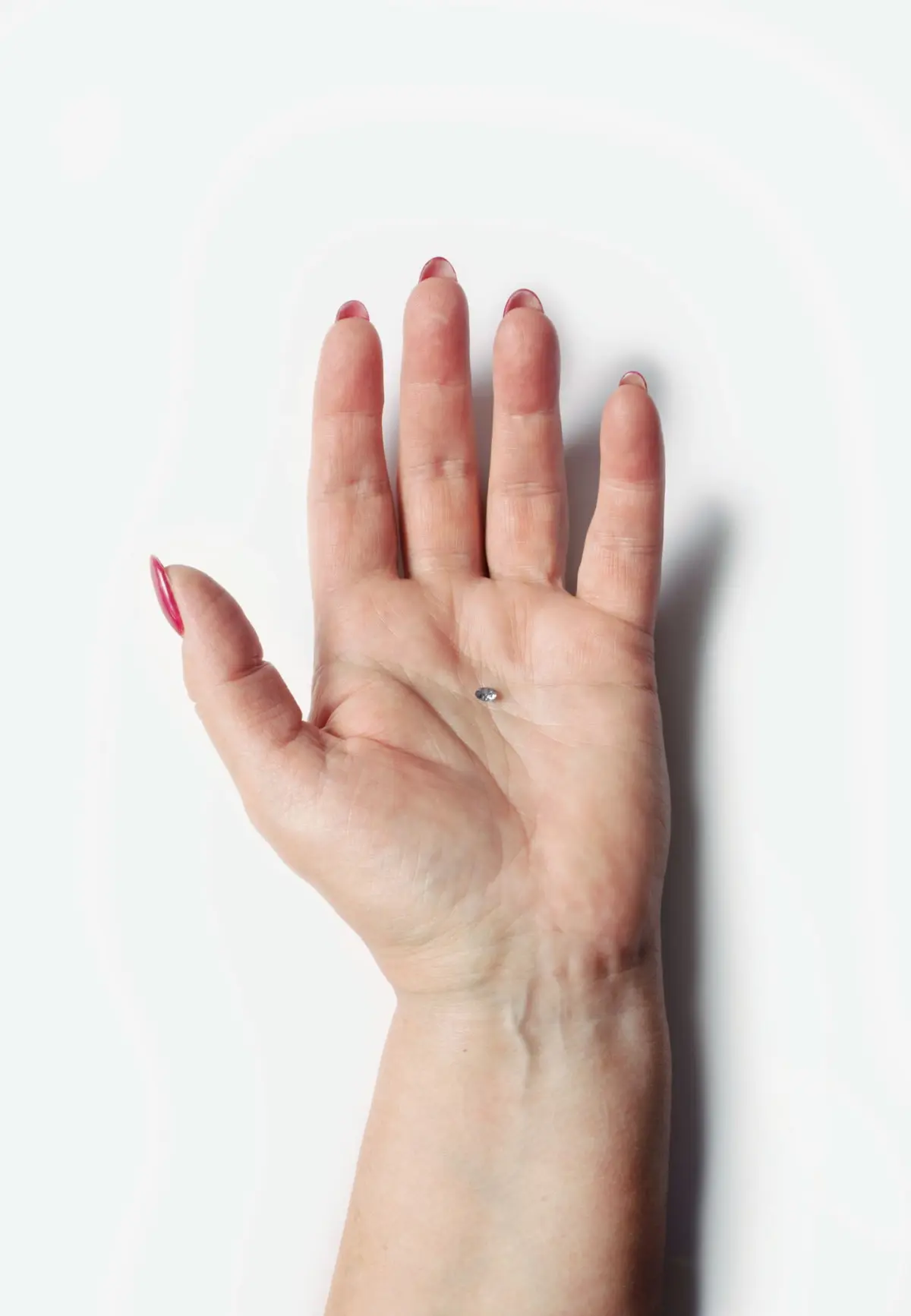 Open adult hand with a small diamond resting on the palm against a white studio background.