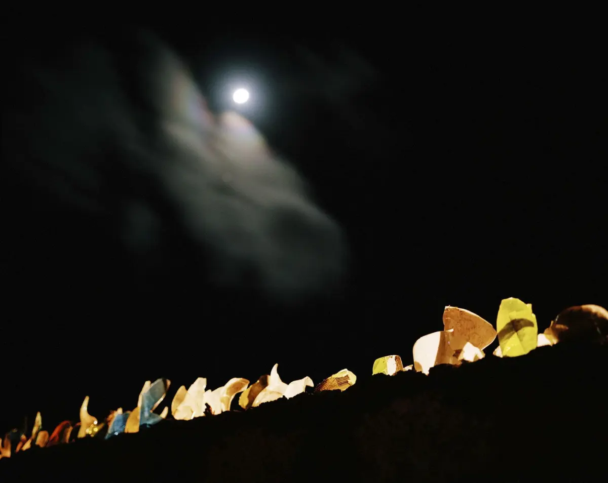 Row of multicolored paper decorations along a ledge at night, with a bright full moon in the dark sky.