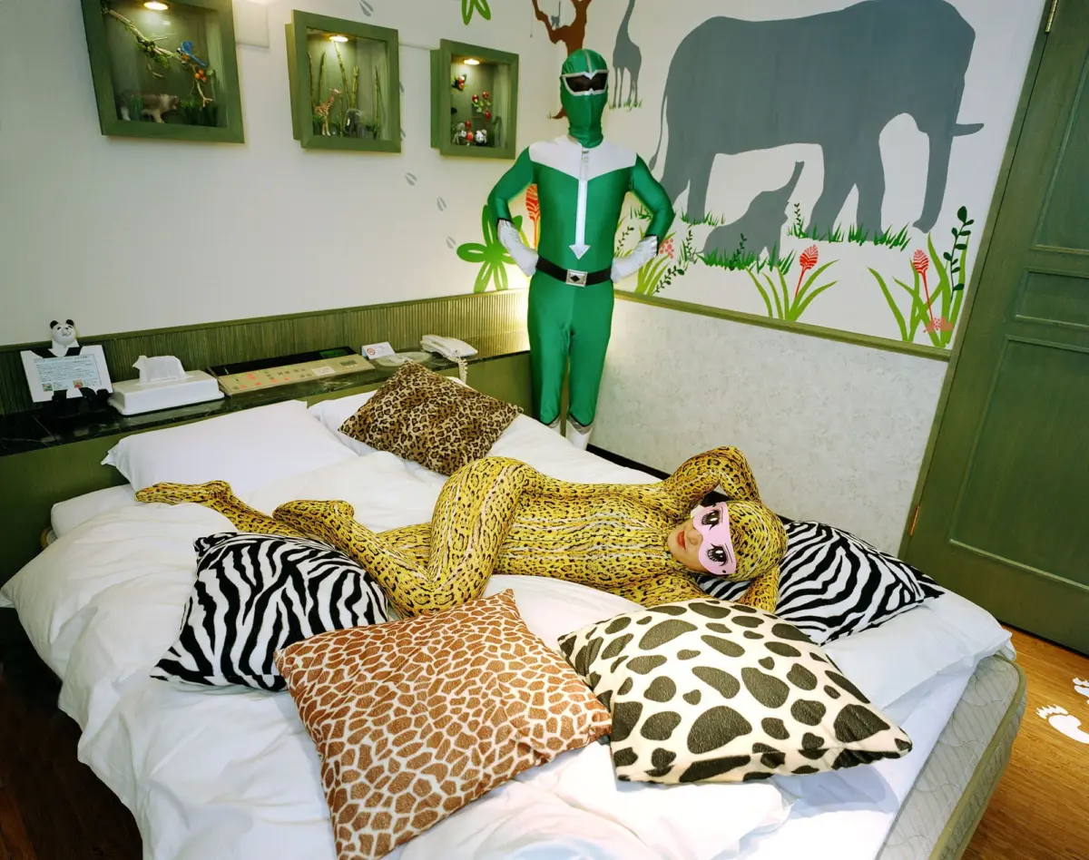 Green Power Ranger stands with hands on hips on a bed; leopard-print costume sprawls on the bedding in a jungle-themed room with an elephant mural.