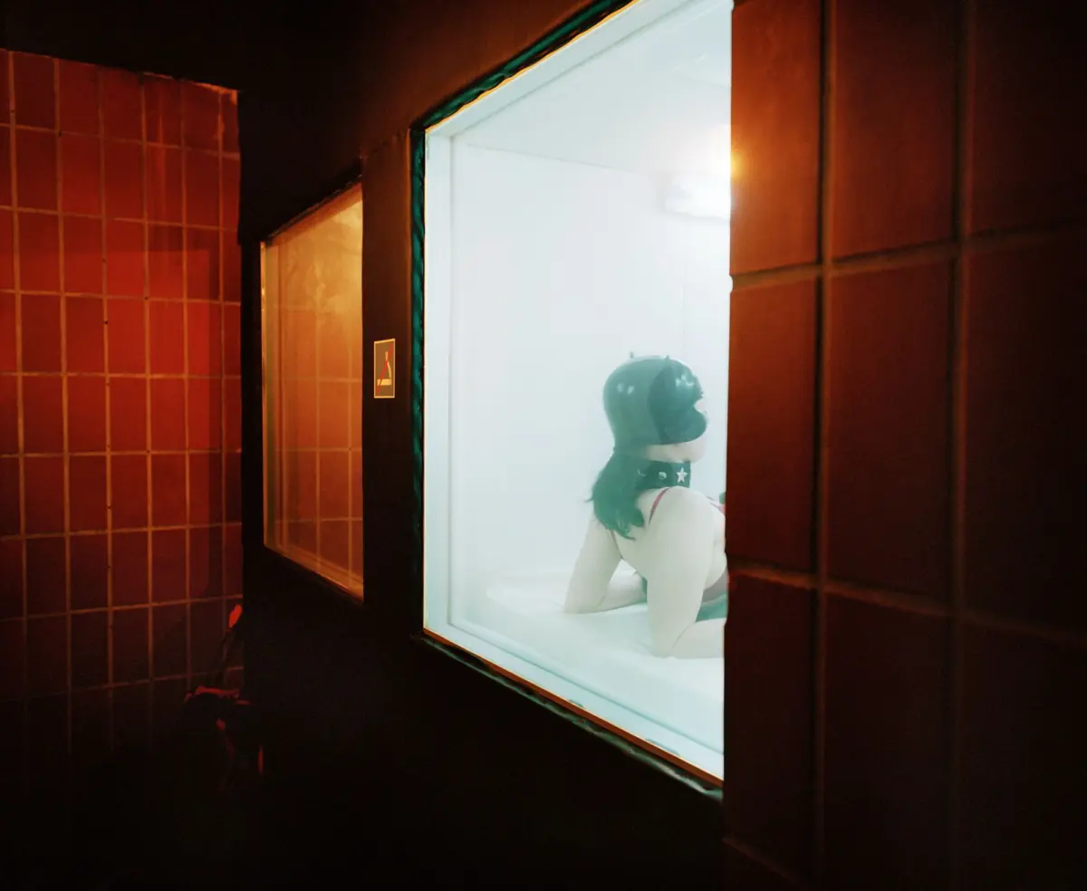 White mannequin wearing helmet posed in brightly lit storefront window, with dark tiled exterior at night.