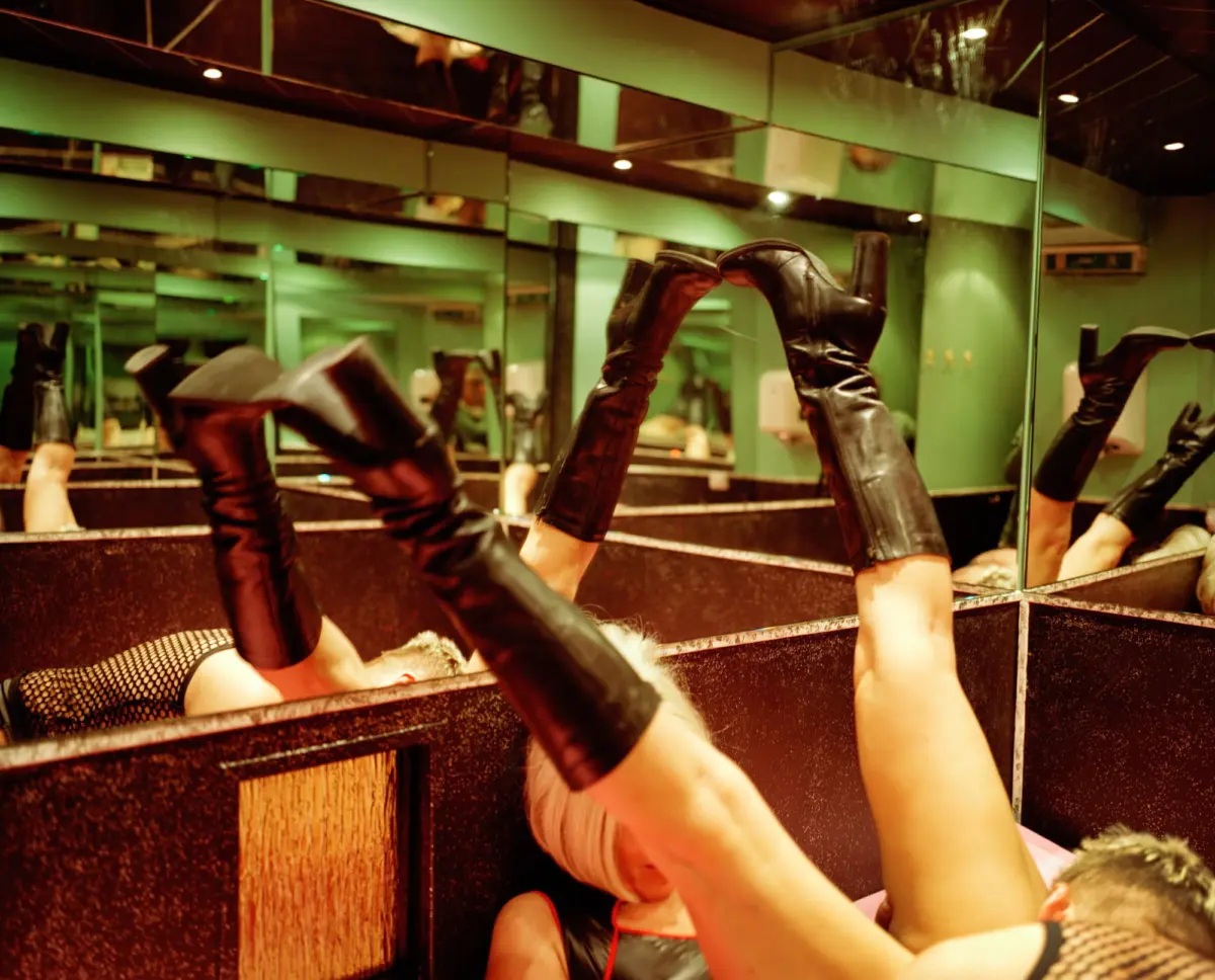 Person wearing black leather thigh-high boots raises legs in a mirror-filled green-walled dressing room