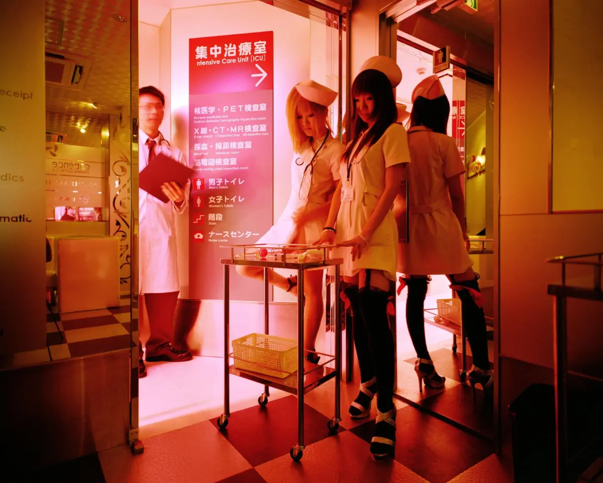 Three nurses in white uniforms and a staff member with clipboard beside an ICU sign in a hospital corridor; serving cart with a yellow basket.
