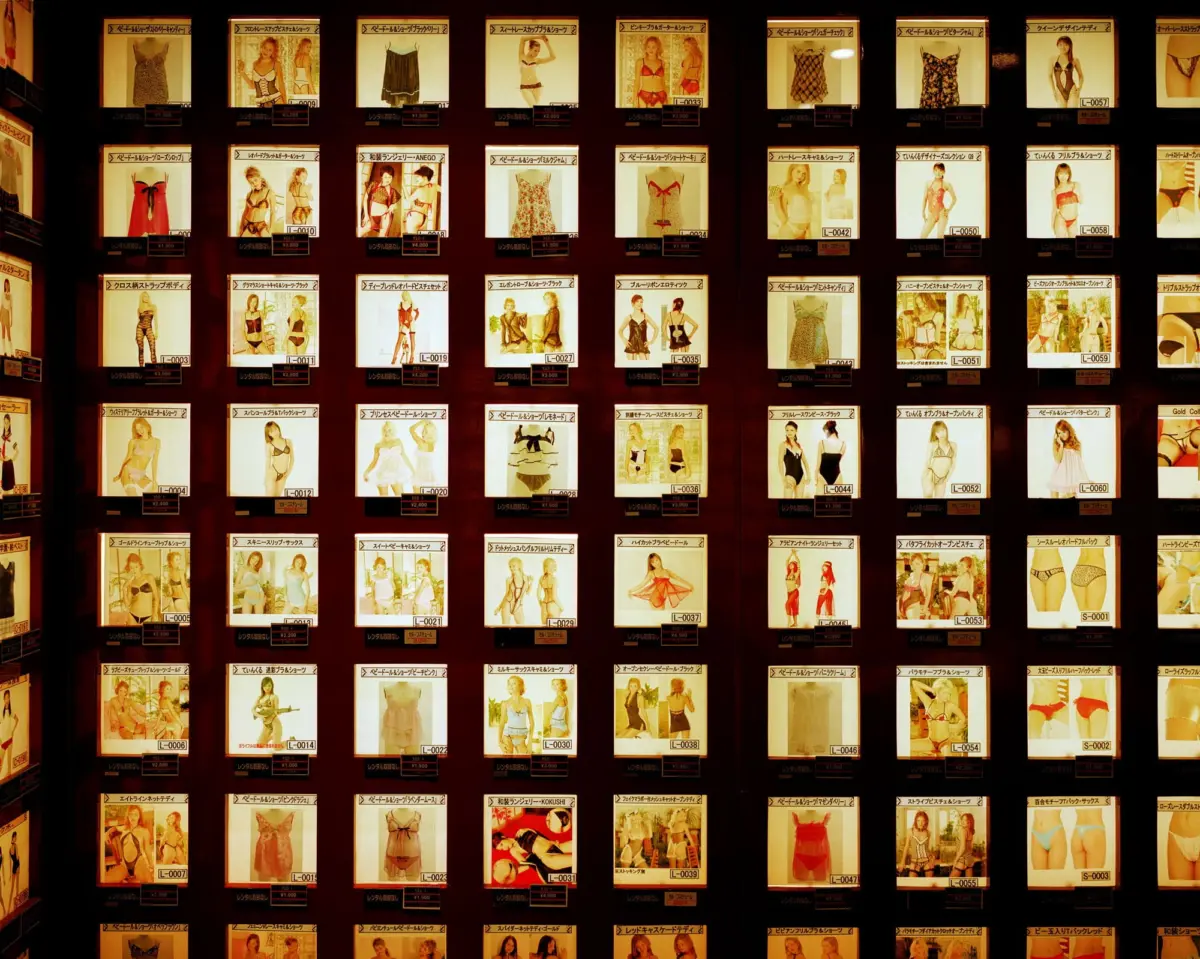 Backlit grid displaying catalog cards of models in lingerie and swimsuits on a dark wall.