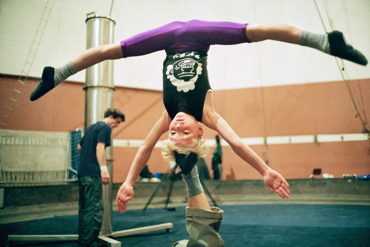 Young gymnast performs a handstand with legs extended in an indoor gym.