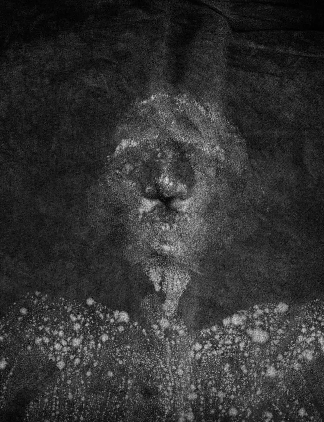 Close-up of dark textured fabric with a pale, elongated stain in the center and dense bubble-like specks along the bottom.