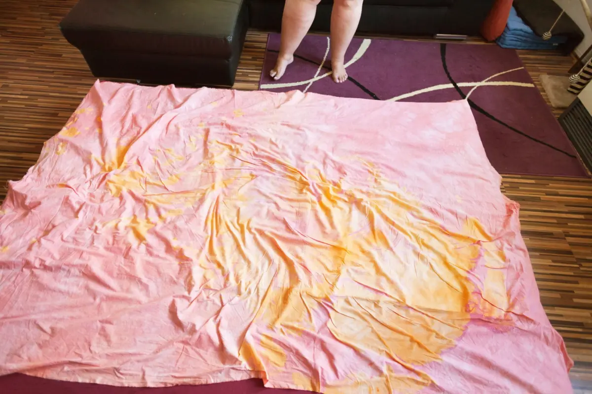 Pink sheet spread on a wooden floor, stained orange; legs visible at the top.