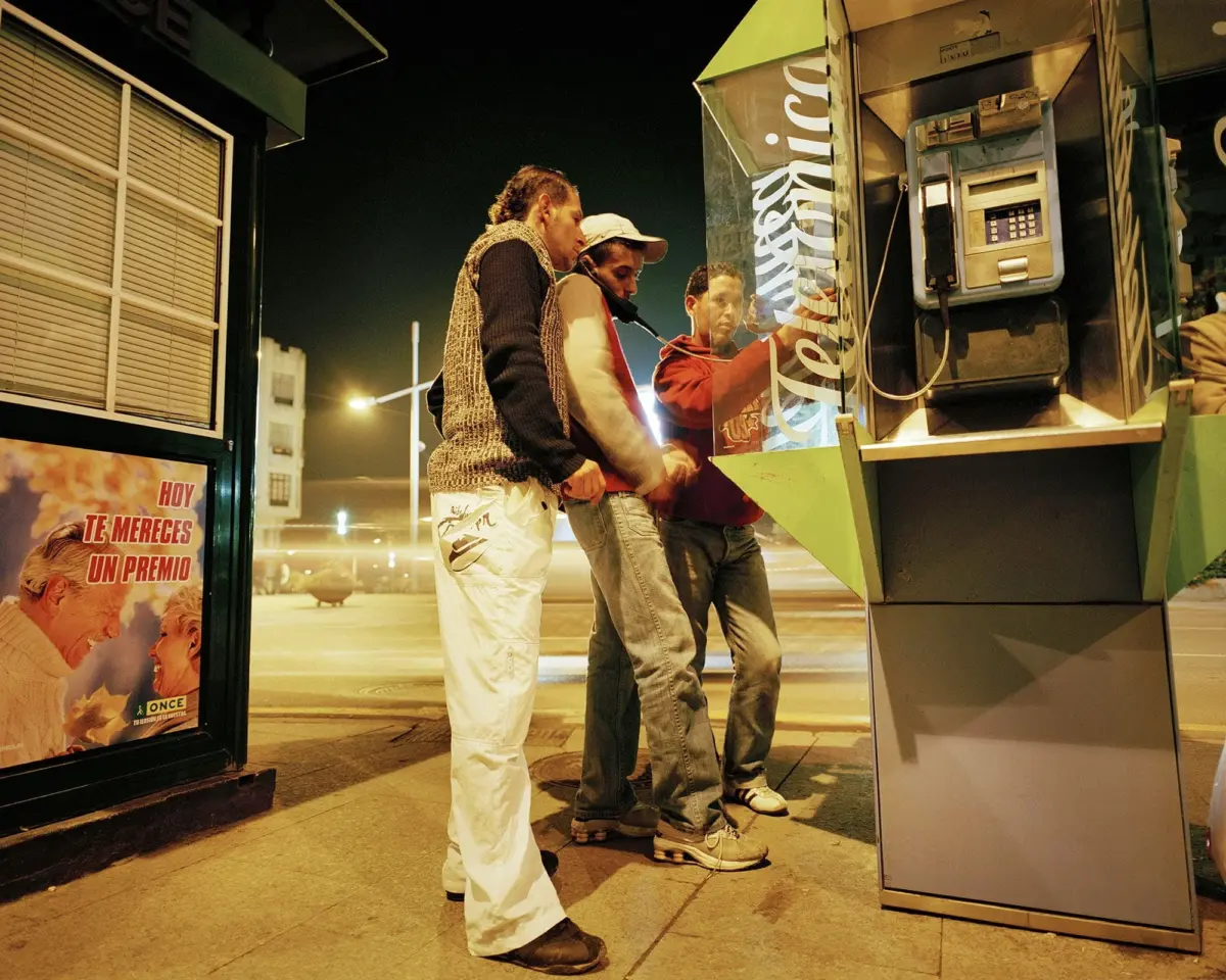 Three men around a street-side ATM at night; one in a red hoodie uses the machine while others watch.