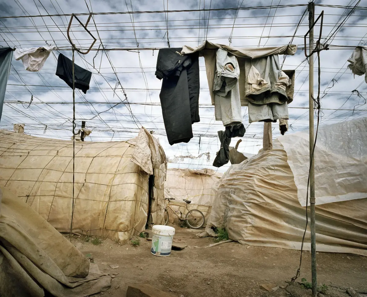 Clothes drying on lines between poles above beige tarps in a dusty outdoor yard; a bicycle visible in the background.