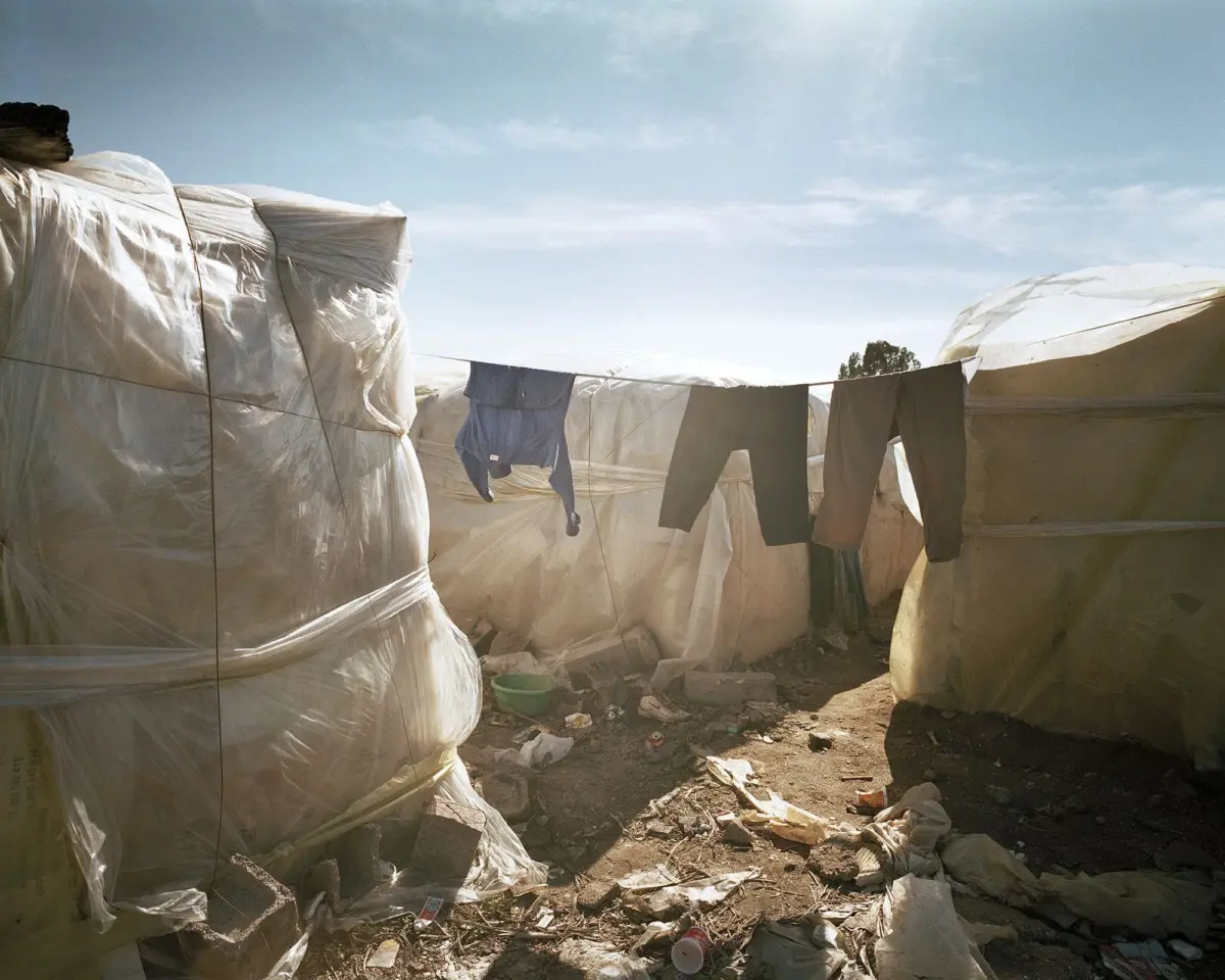 Desert makeshift camp with white plastic tents; clothing hangs on a line between shelters.