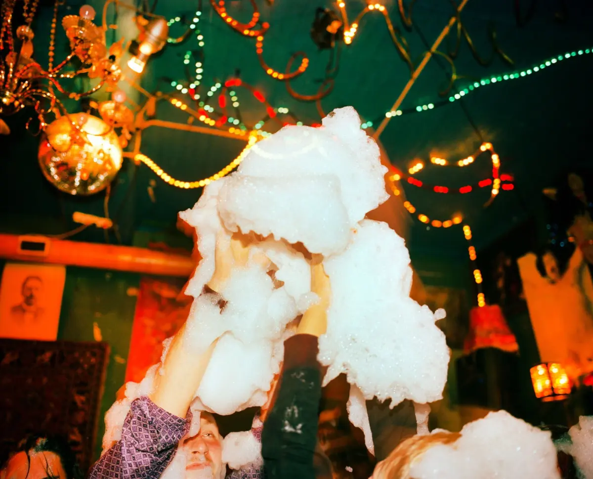 Person lifts large snow sculpture at a festive indoor event, with colorful string lights and a disco ball in background.