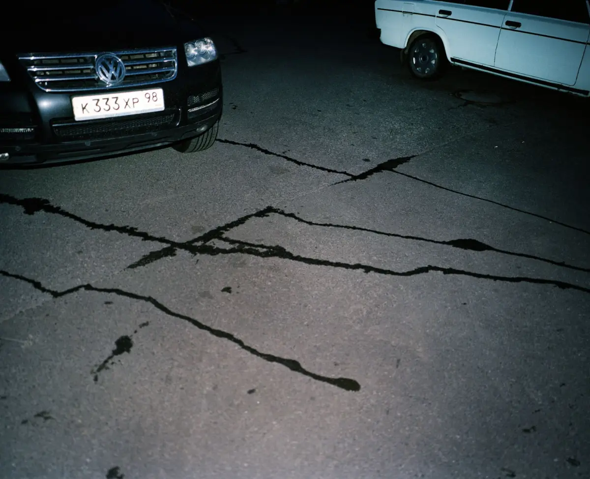 Two parked vehicles: a black Volkswagen SUV and a white cargo van, on cracked asphalt at night.
