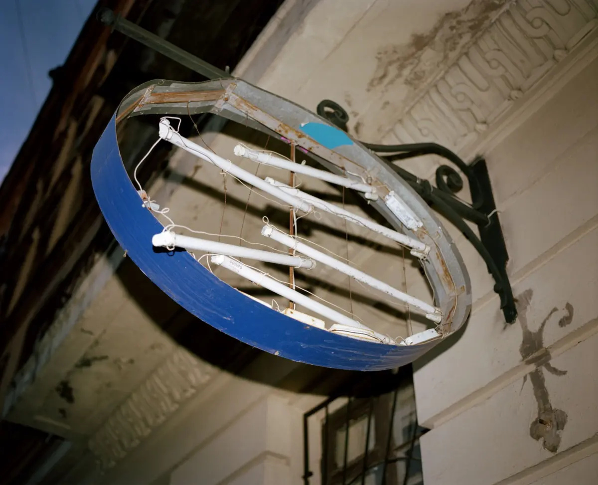 Rusty circular metal light fixture with fluorescent tubes, hanging in a crumbling interior with peeling walls and ornate railing.
