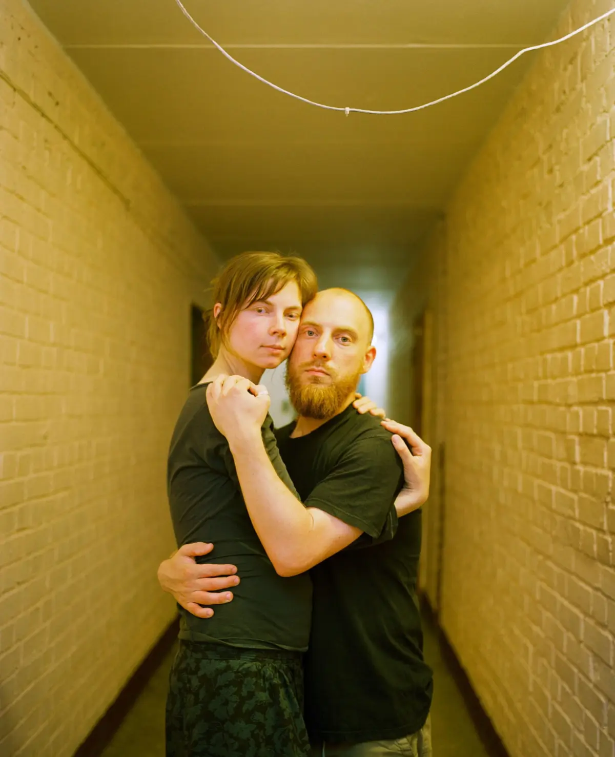 Adult couple embracing in a narrow brick hallway, facing the camera.