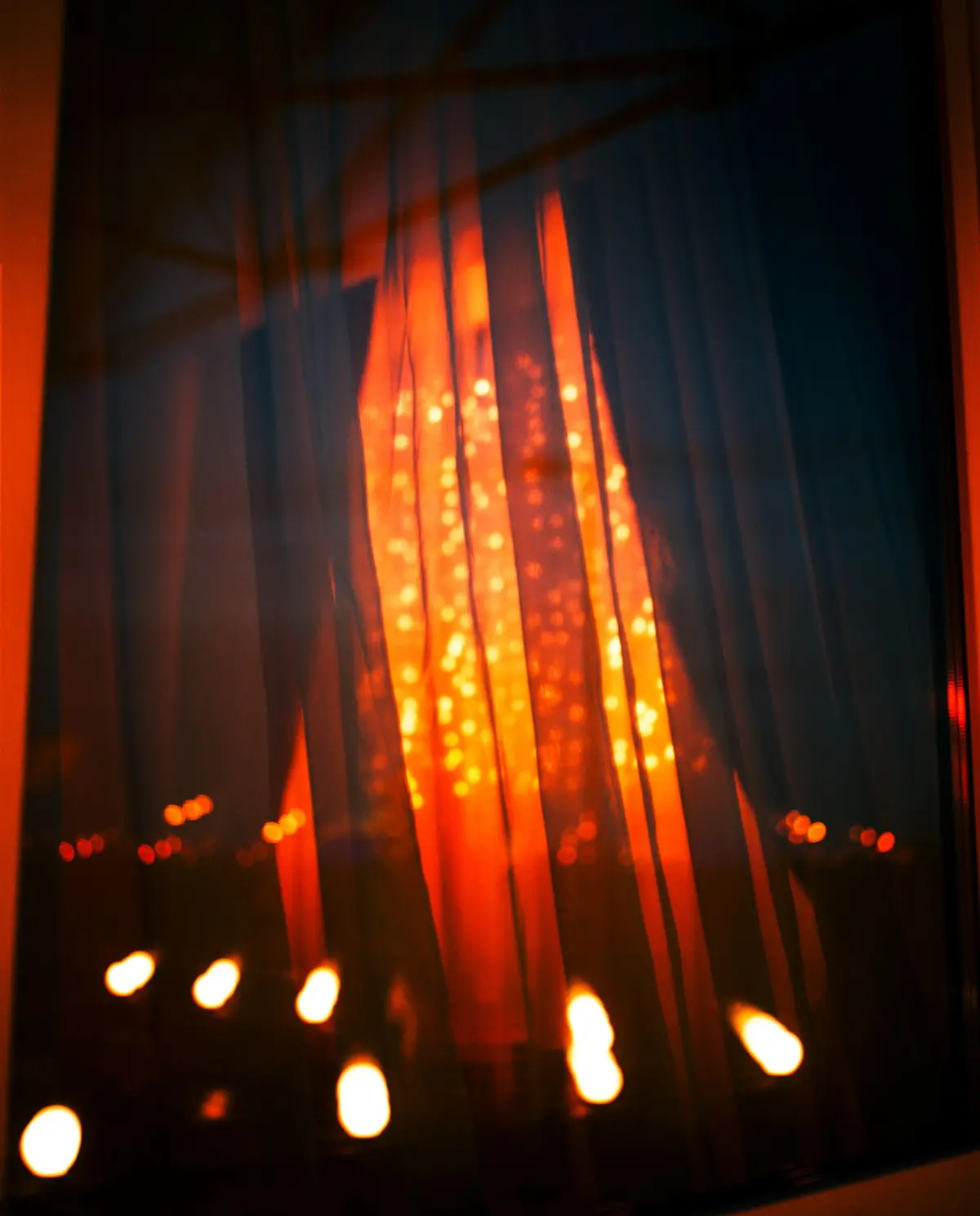 Blurry view through vertical blinds with glowing orange lights behind, suggesting a nighttime cityscape.