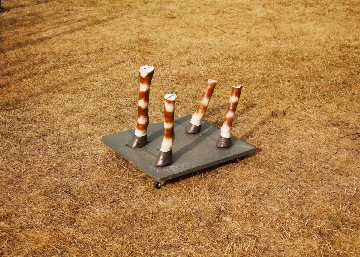 Four striped birch-log sculptures protruding from a gray wheeled platform in a dry, yellow-brown field.