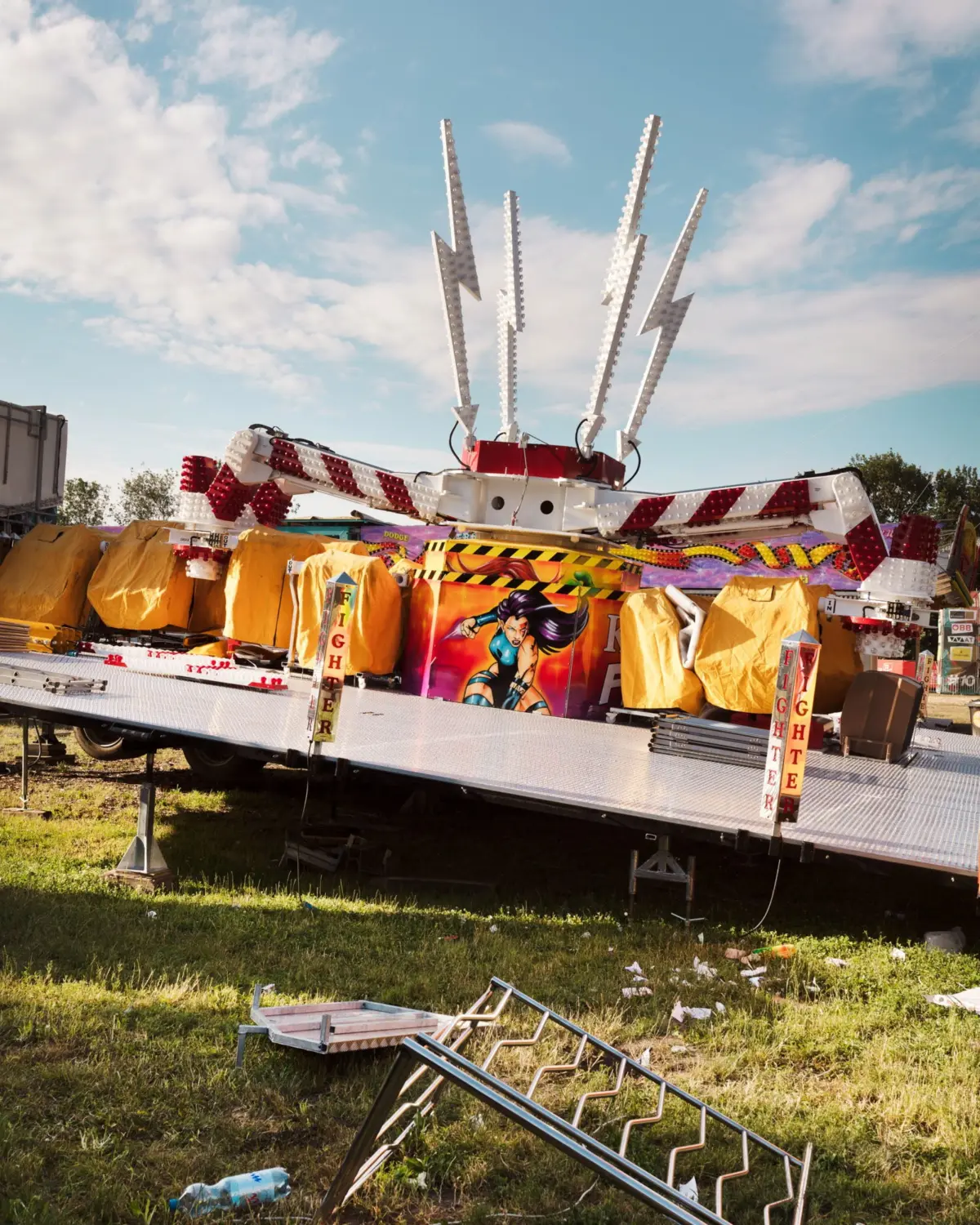 Carnival ride with tall white LED-lit arms upright on a flatbed trailer at an outdoor fairground.