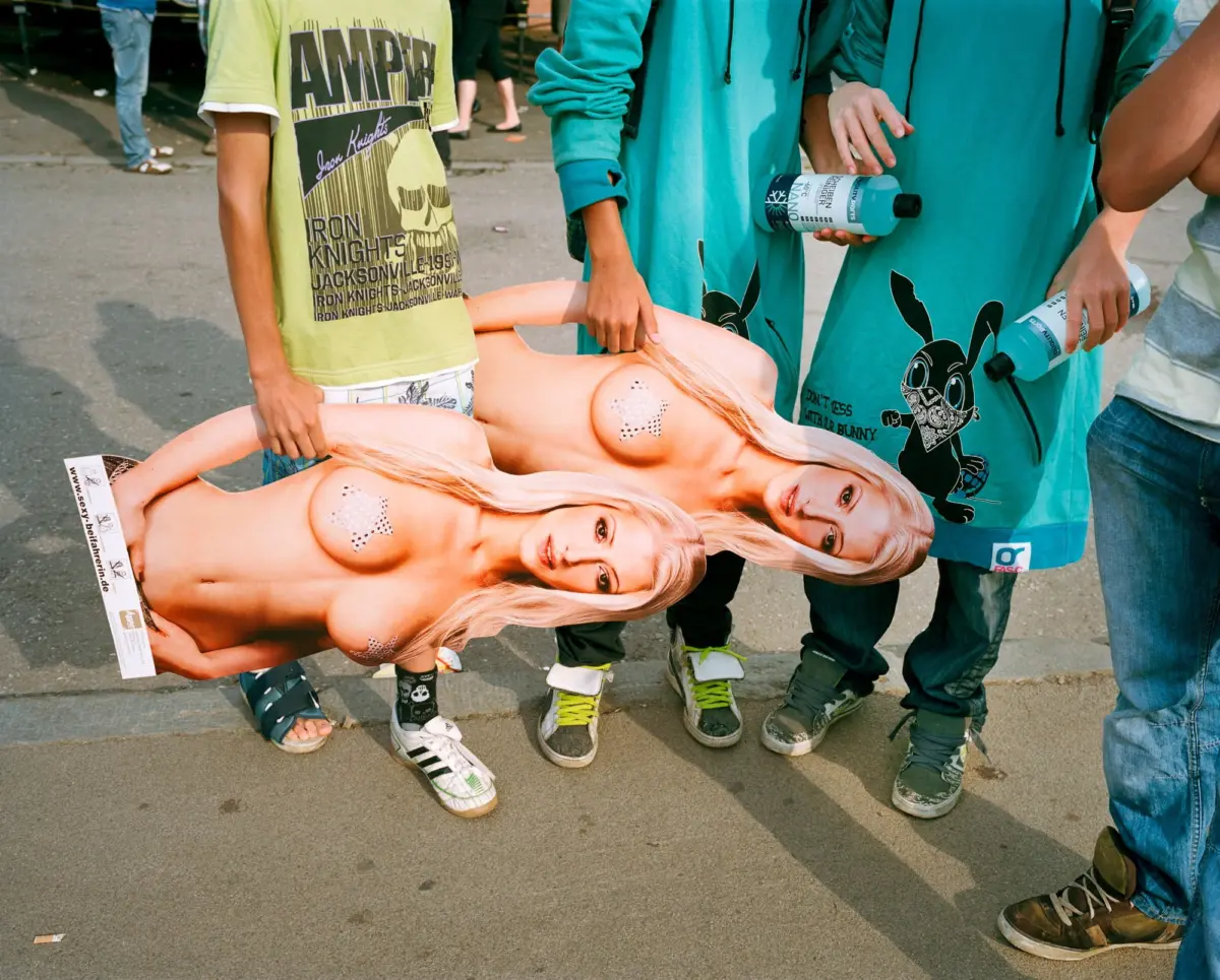 Life-size poster of a nude blonde woman lying on pavement, surrounded by people in turquoise outfits holding water bottles.