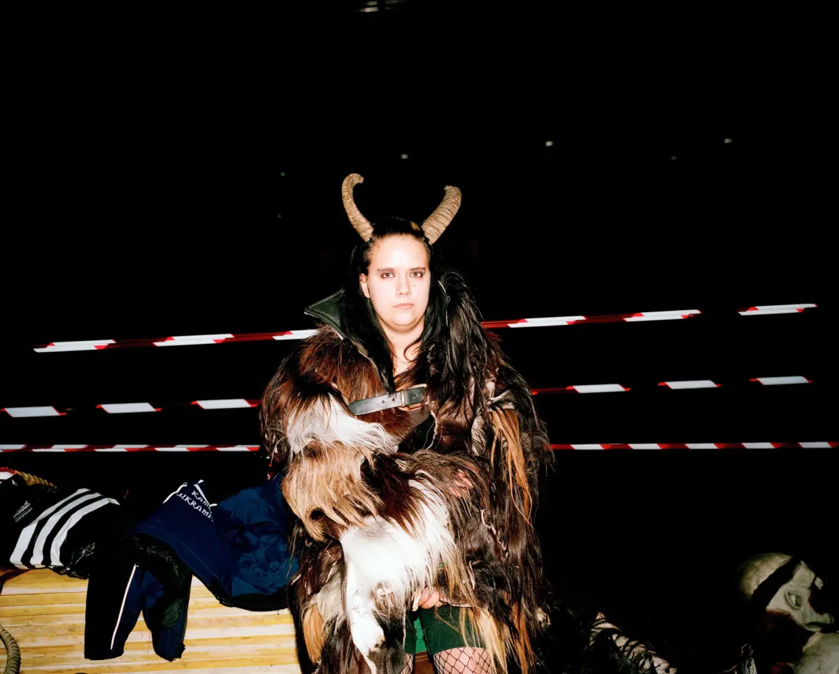 Person in ram-horned fur costume posing against dark background with red-and-white barrier tape.