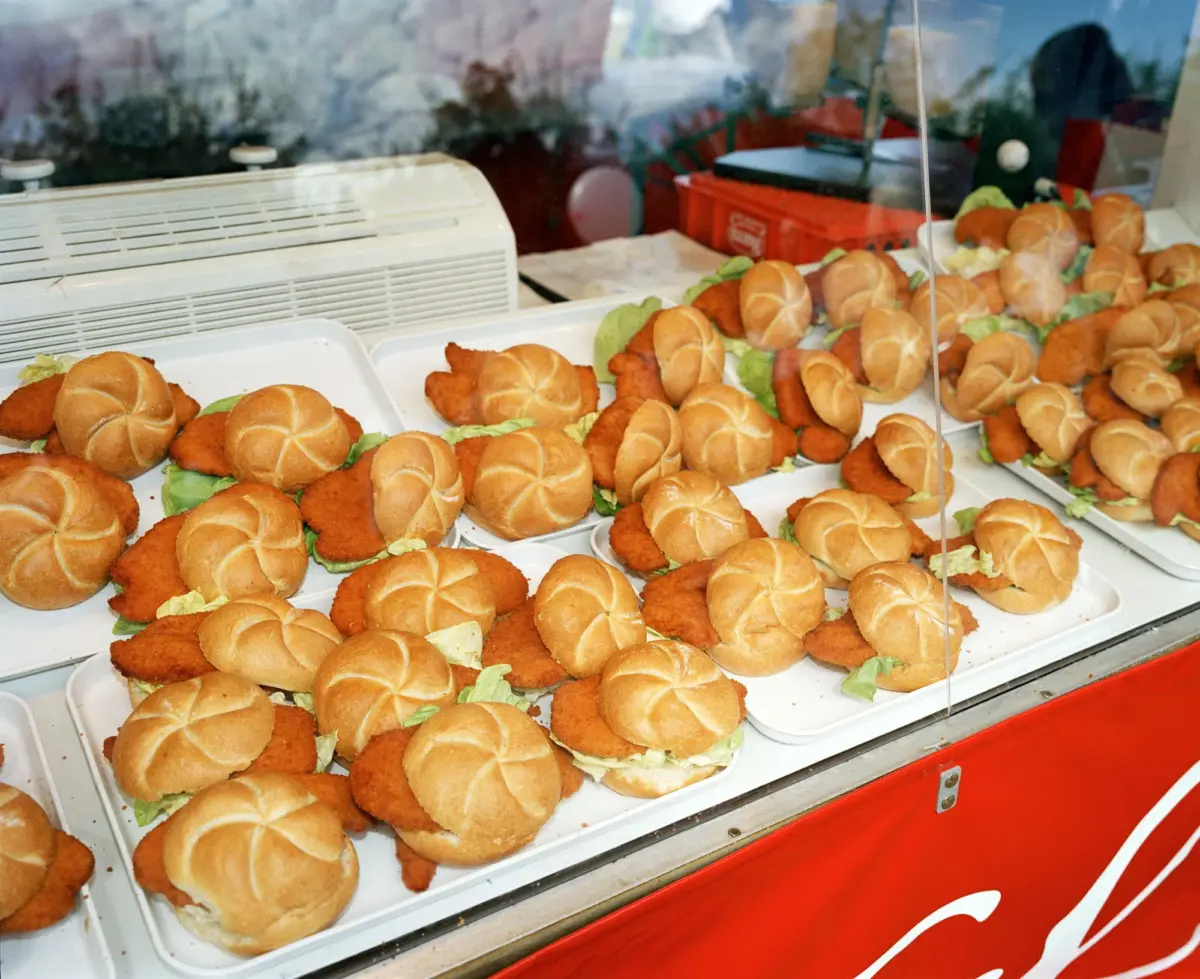 Rows of breaded chicken sandwiches with lettuce in a glass display at a fast-food counter.