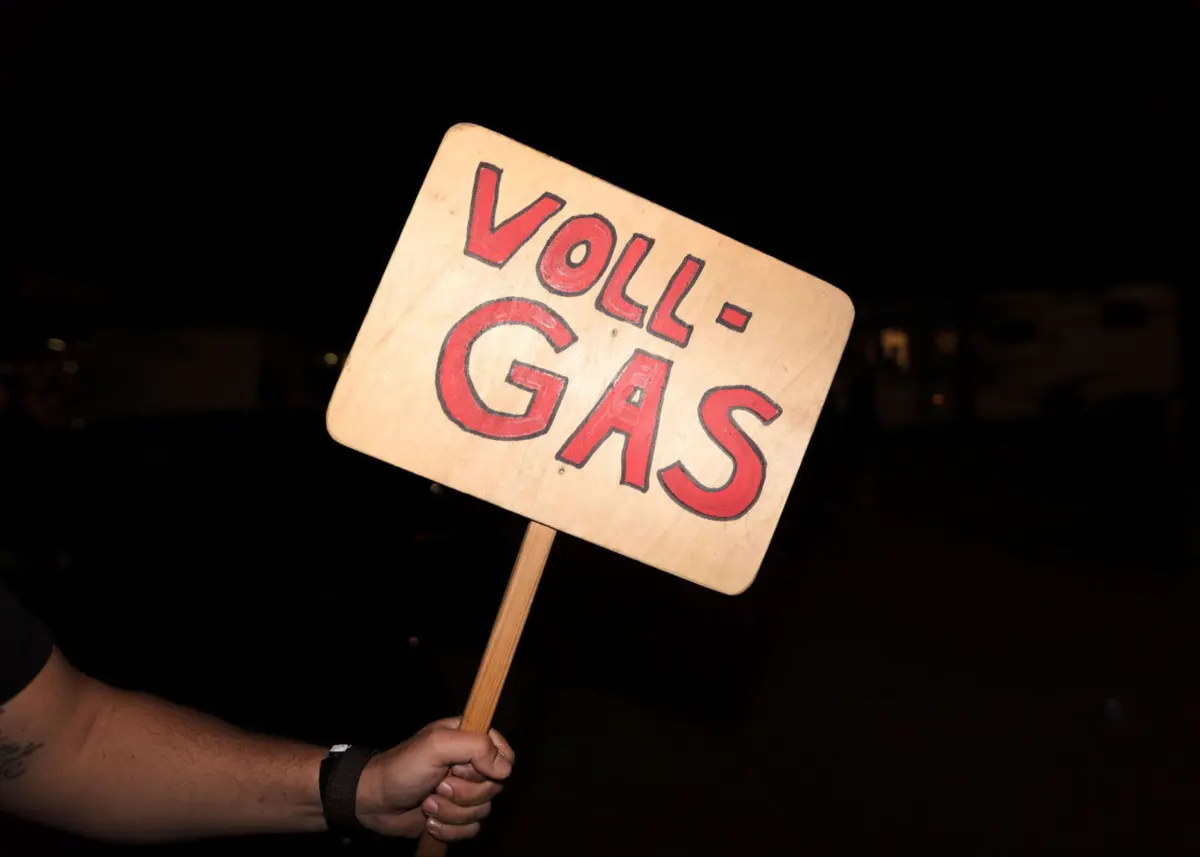 Wooden protest sign reading 'VOLL GAS' held by a person at night.