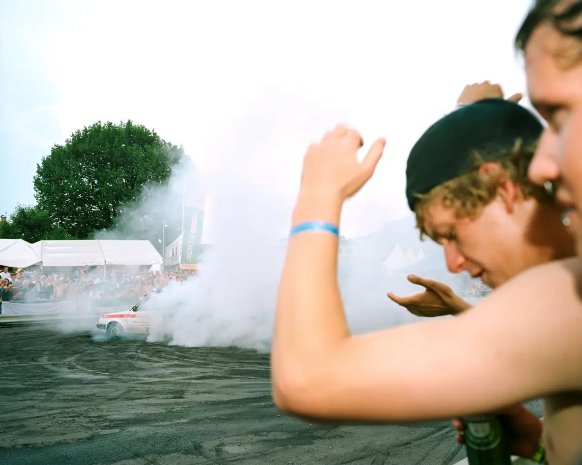 Drift car emits smoke as crowd watches at an outdoor festival with tents.
