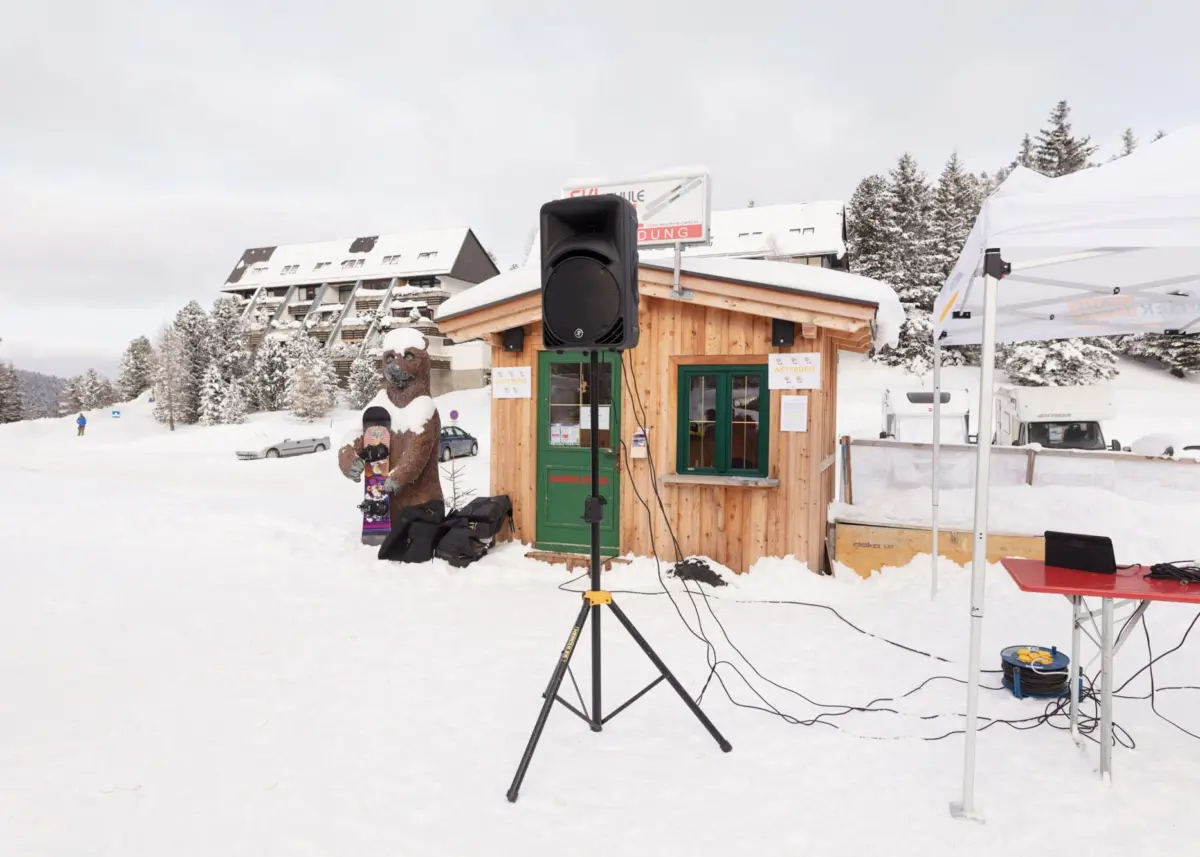 Loudspeaker on tripod in front of a wooden booth at snowy ski resort.